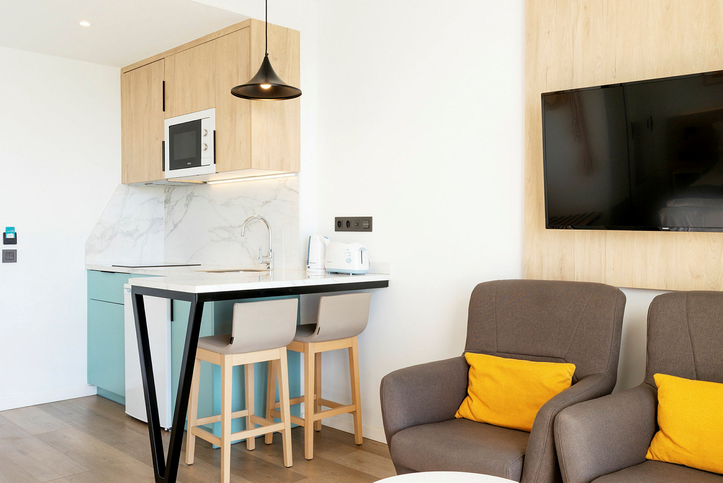 Modernt kök med sittplats och vardagsrum med stolar och en väggmonterad TV. (AI-genererad text)
