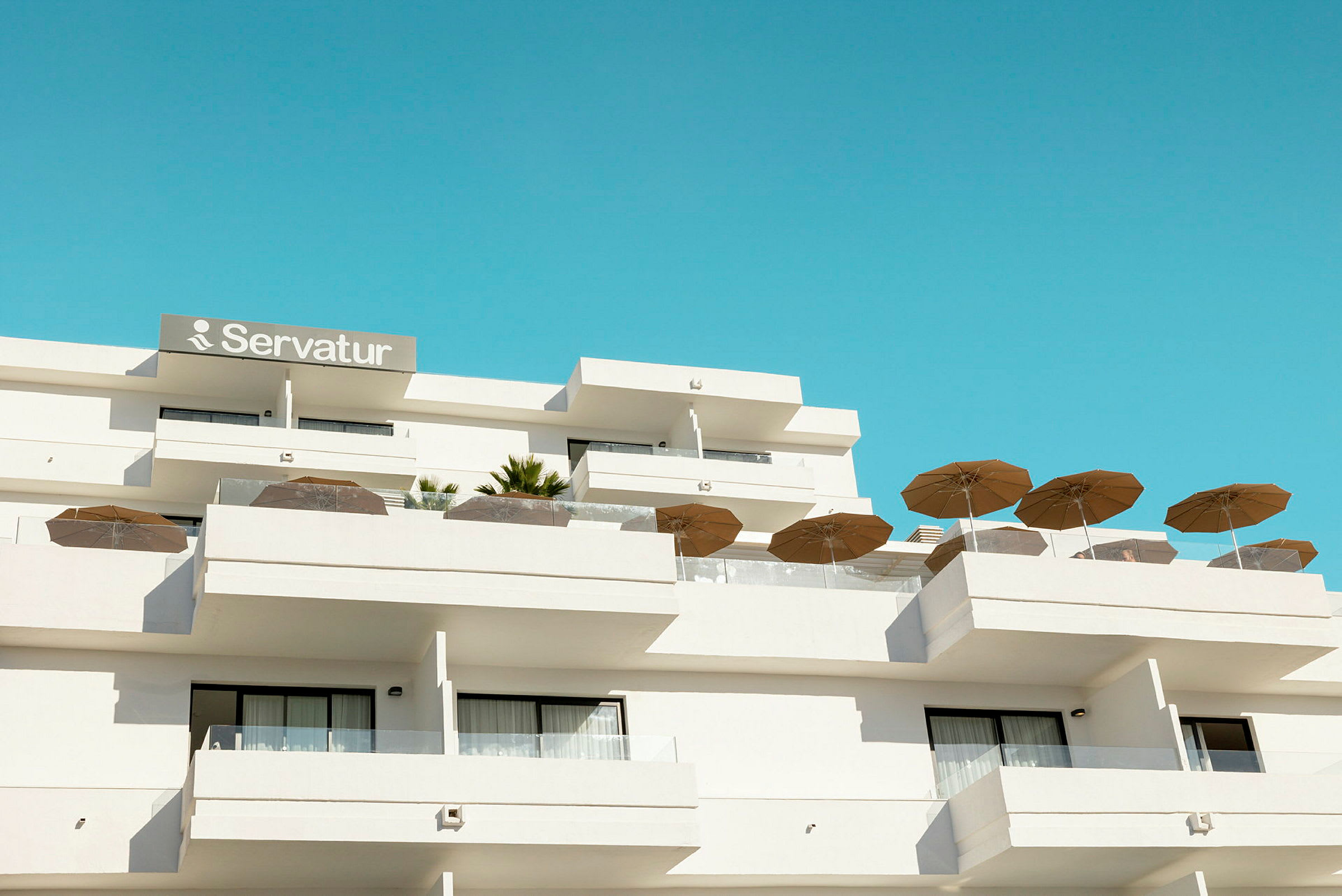 Hotellbyggnad med balkonger och parasoller mot en blå himmel. (AI-genererad text)