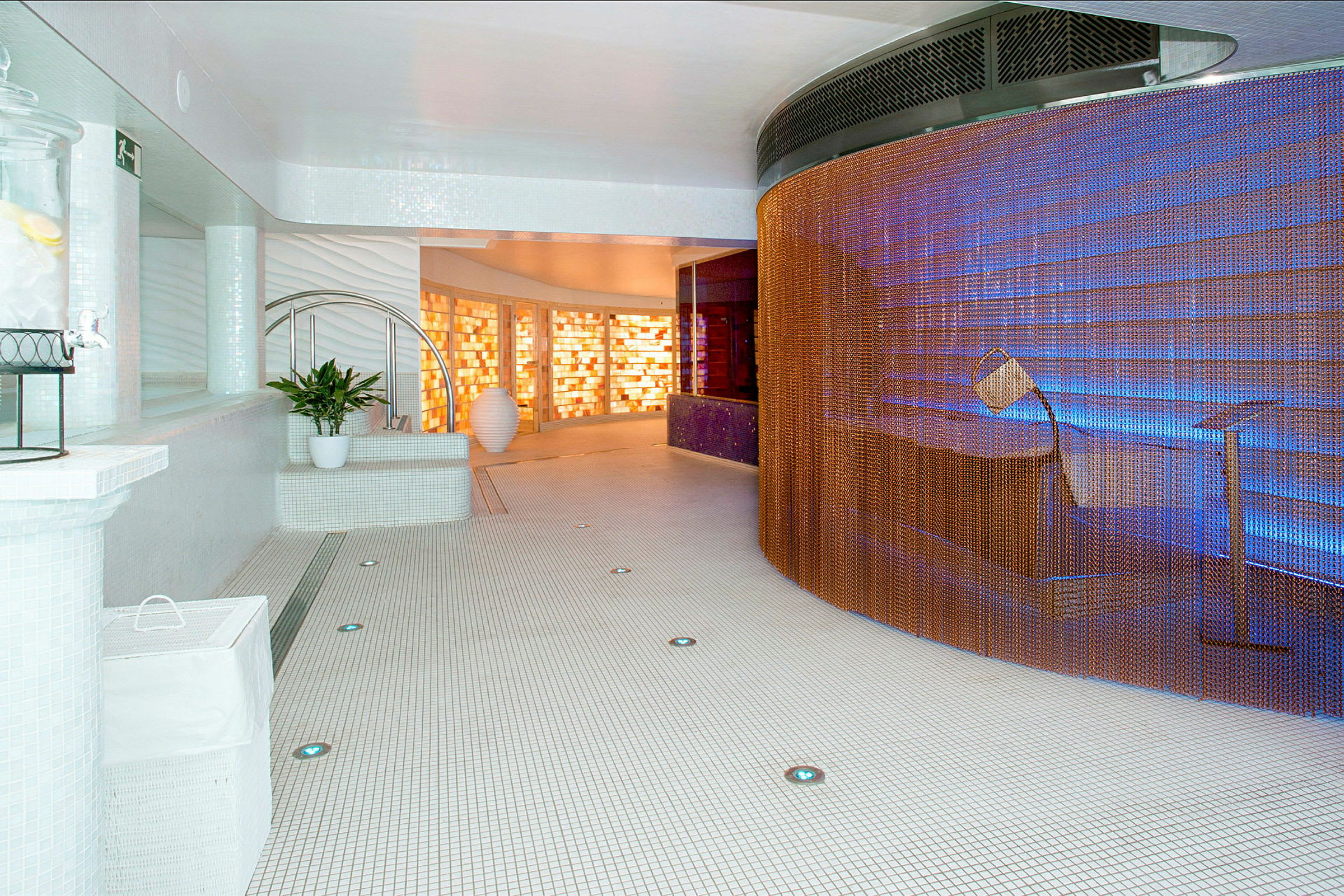 En modern spa-anläggning med vita kakelväggar och golv, orange skärmar och mjuk belysning. (AI-genererad text)