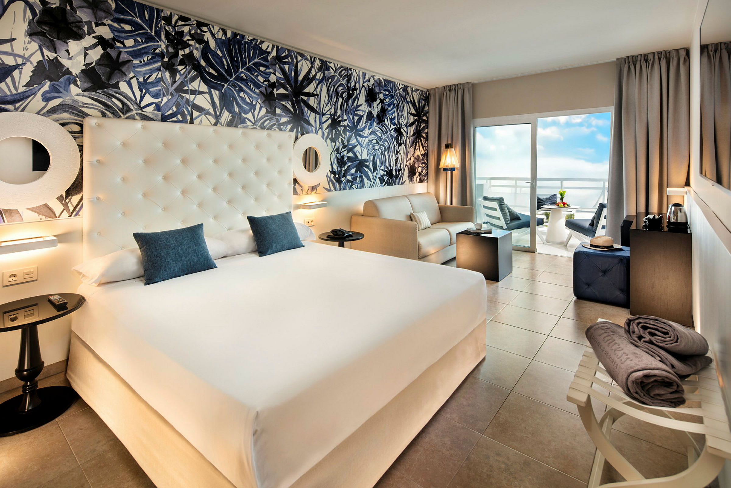 Hotellrum med en stor säng, sittgrupp och balkong med utsikt. (AI-genererad text)