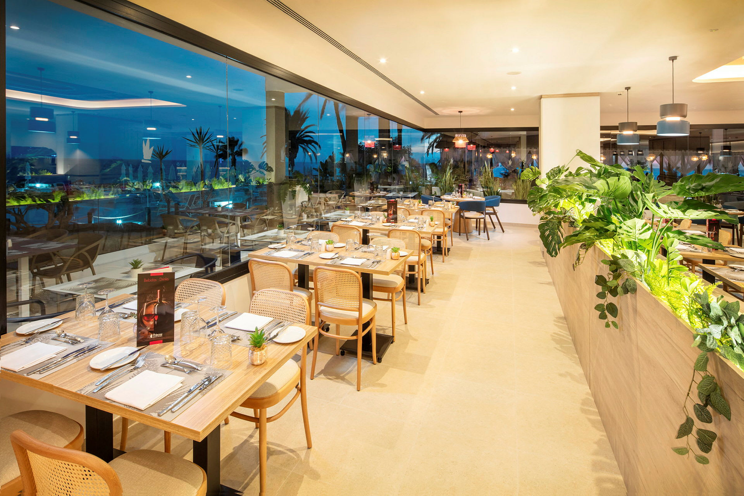 En restaurang med dukade bord och utsikt över utomhusområde genom glasvägg. (AI-genererad text)