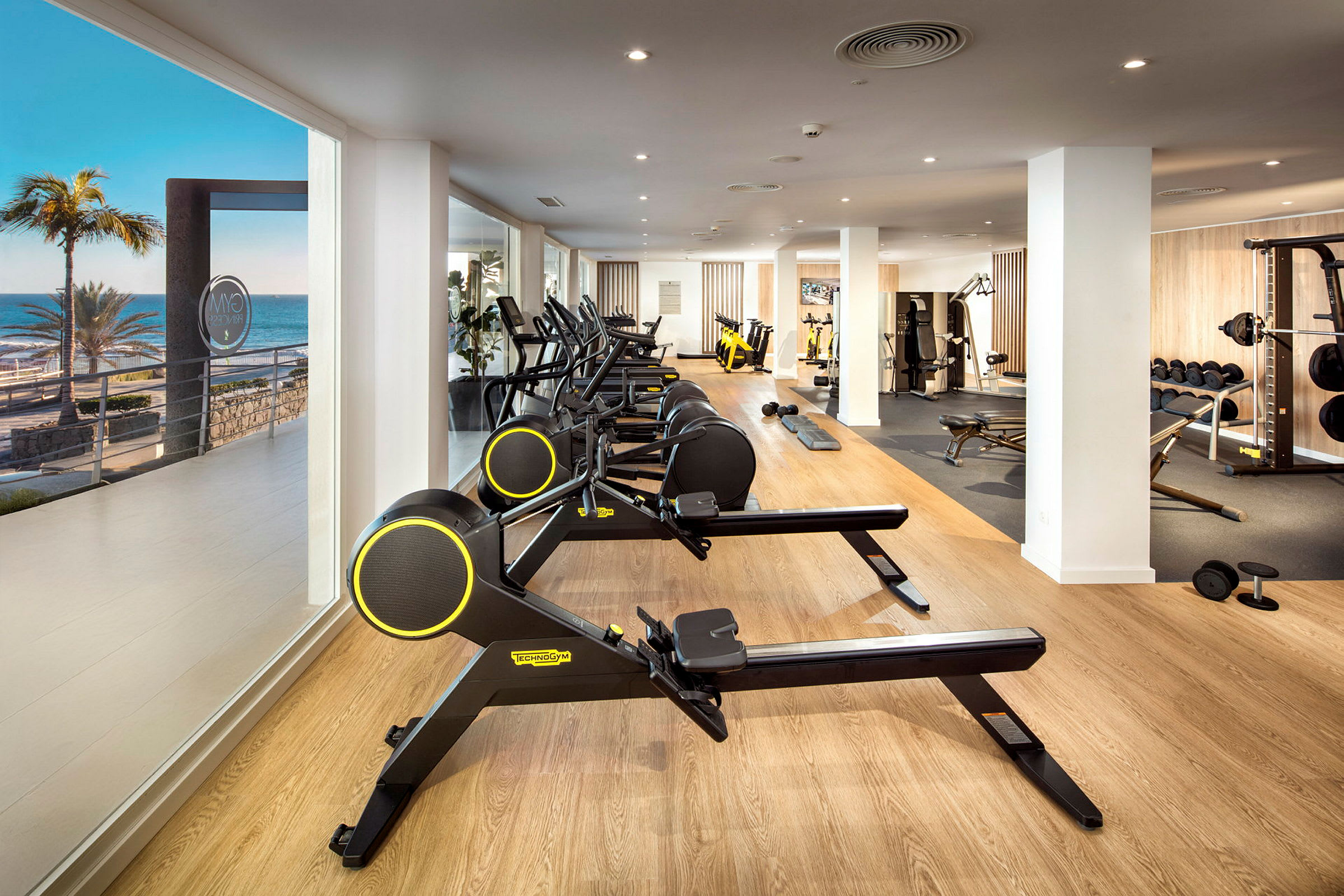 Gym med träningsmaskiner och havsutsikt genom fönstret. (AI-genererad text)