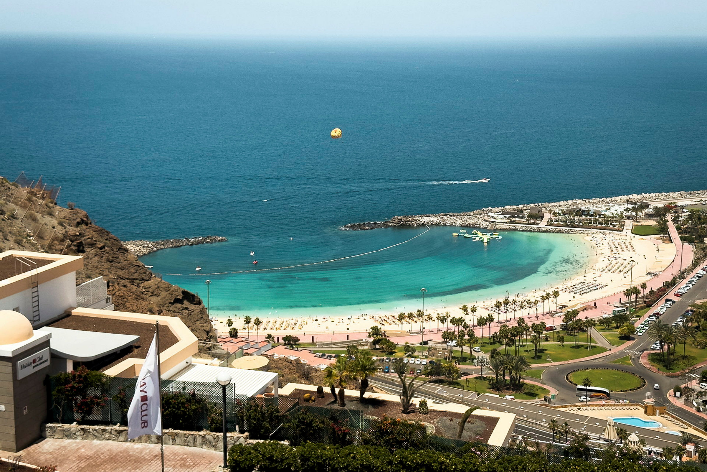 Utsikt över en strand med turkost vatten, solstolar och parasoller samt hotellbyggnader. (AI-genererad text)
