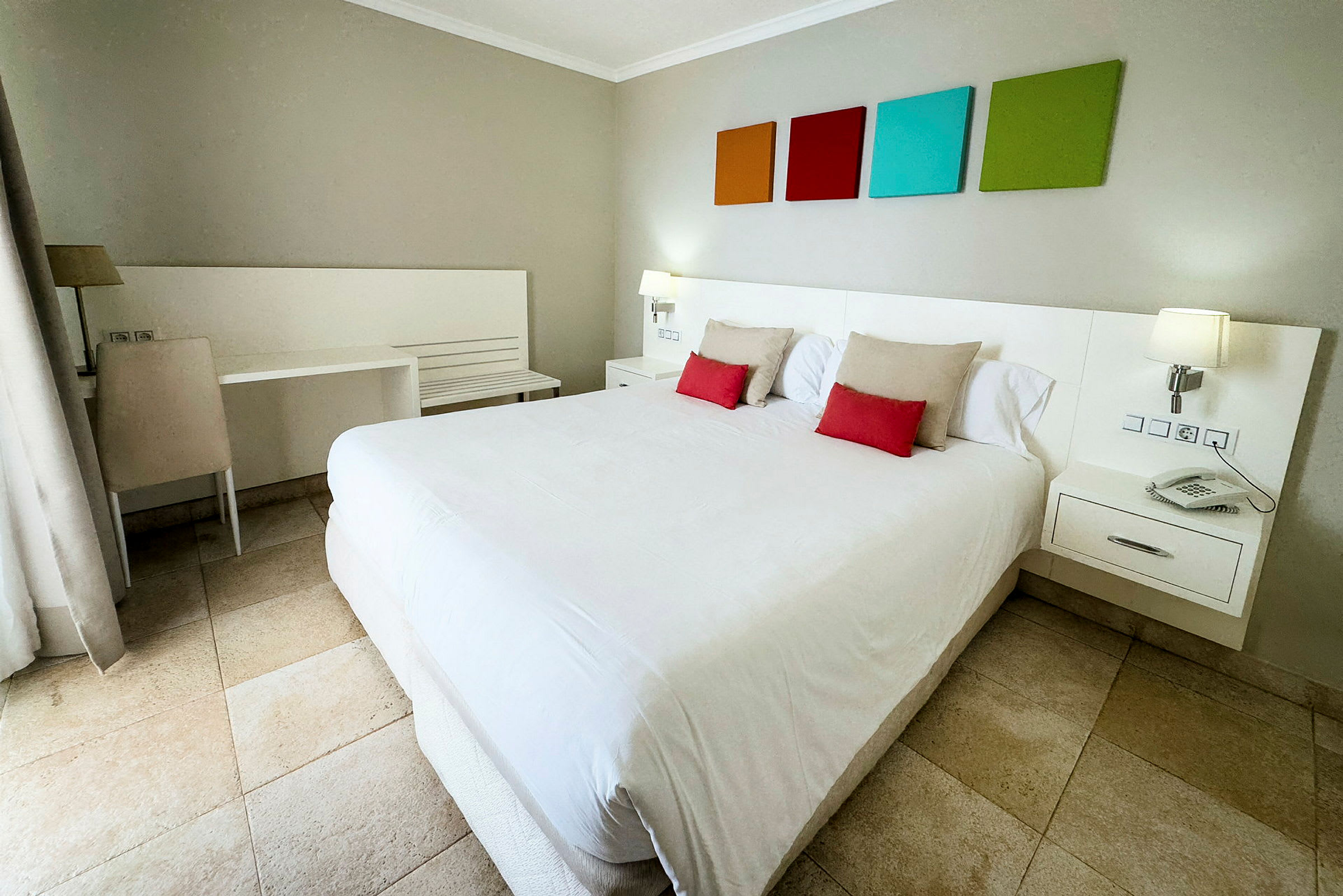 Ett hotellrum med en stor dubbelsäng, färgglada dekorationer på väggen och ljusa möbler. (AI-genererad text)