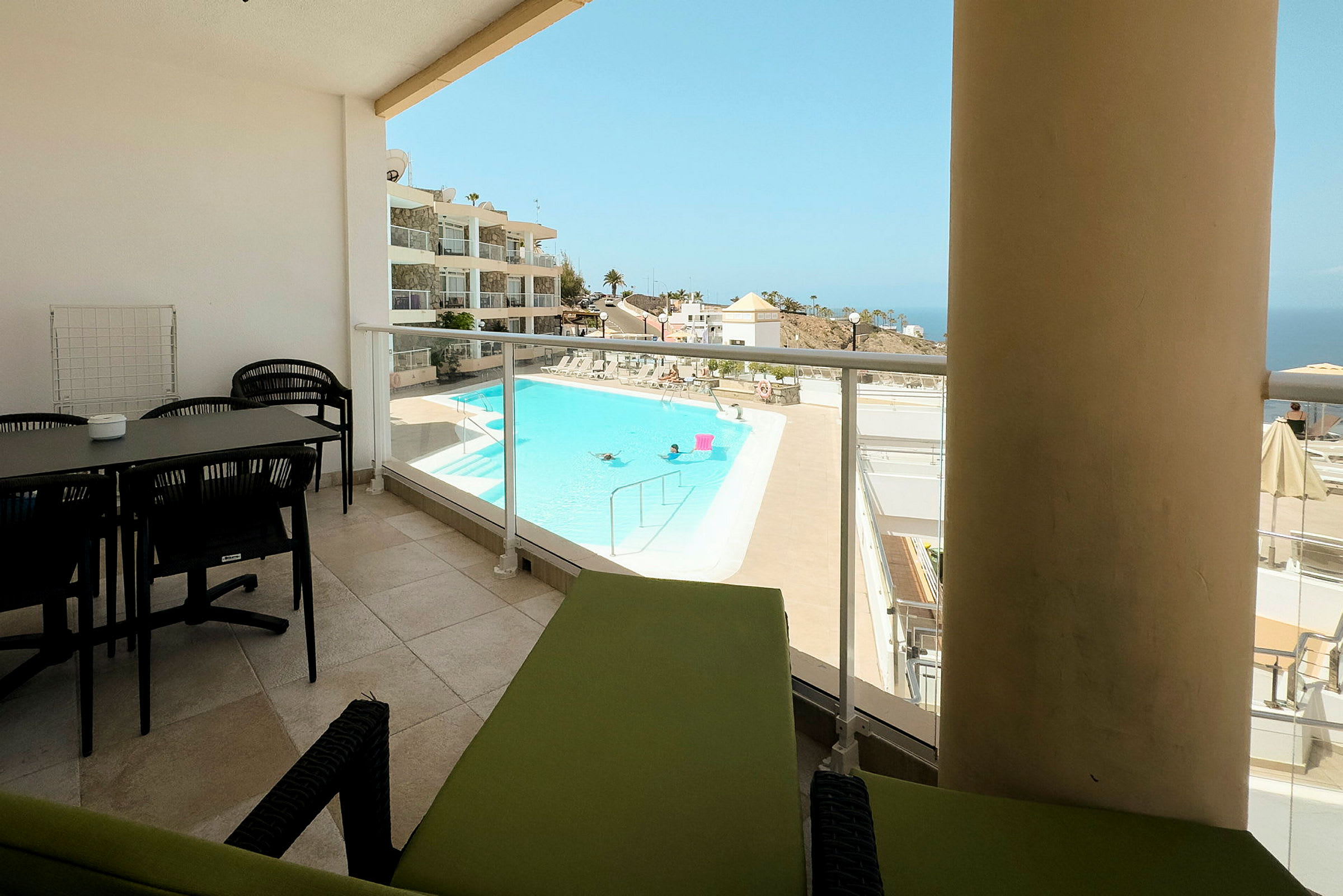 En terrass med bord och stolar samt en utsikt över en pool och omgivande byggnader. (AI-genererad text)