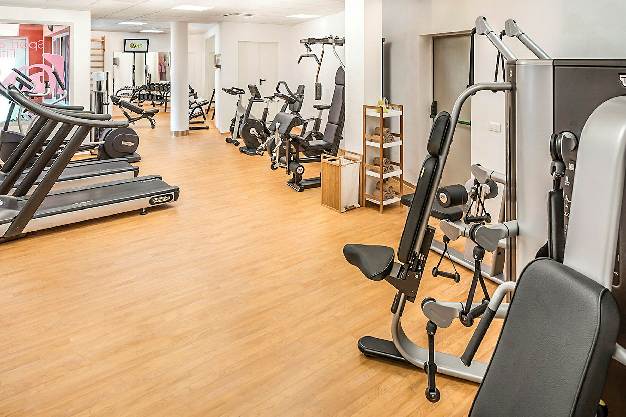 Ett gym med träningsmaskiner, löpband och cyklar på ett trägolv. (AI-genererad text)
