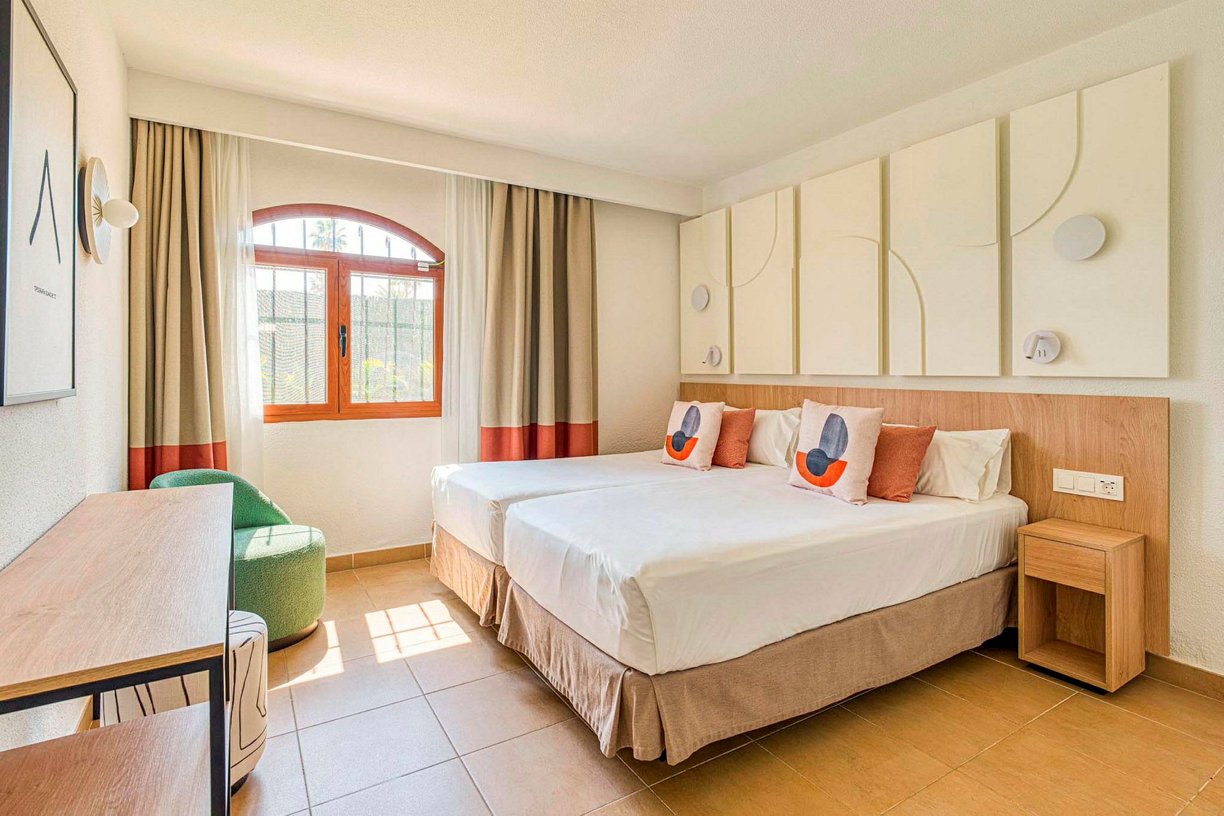 Ett ljust och modernt inrett hotellrum med två enkelsängar, en fönstervy och dekorativa element. (AI-genererad text)