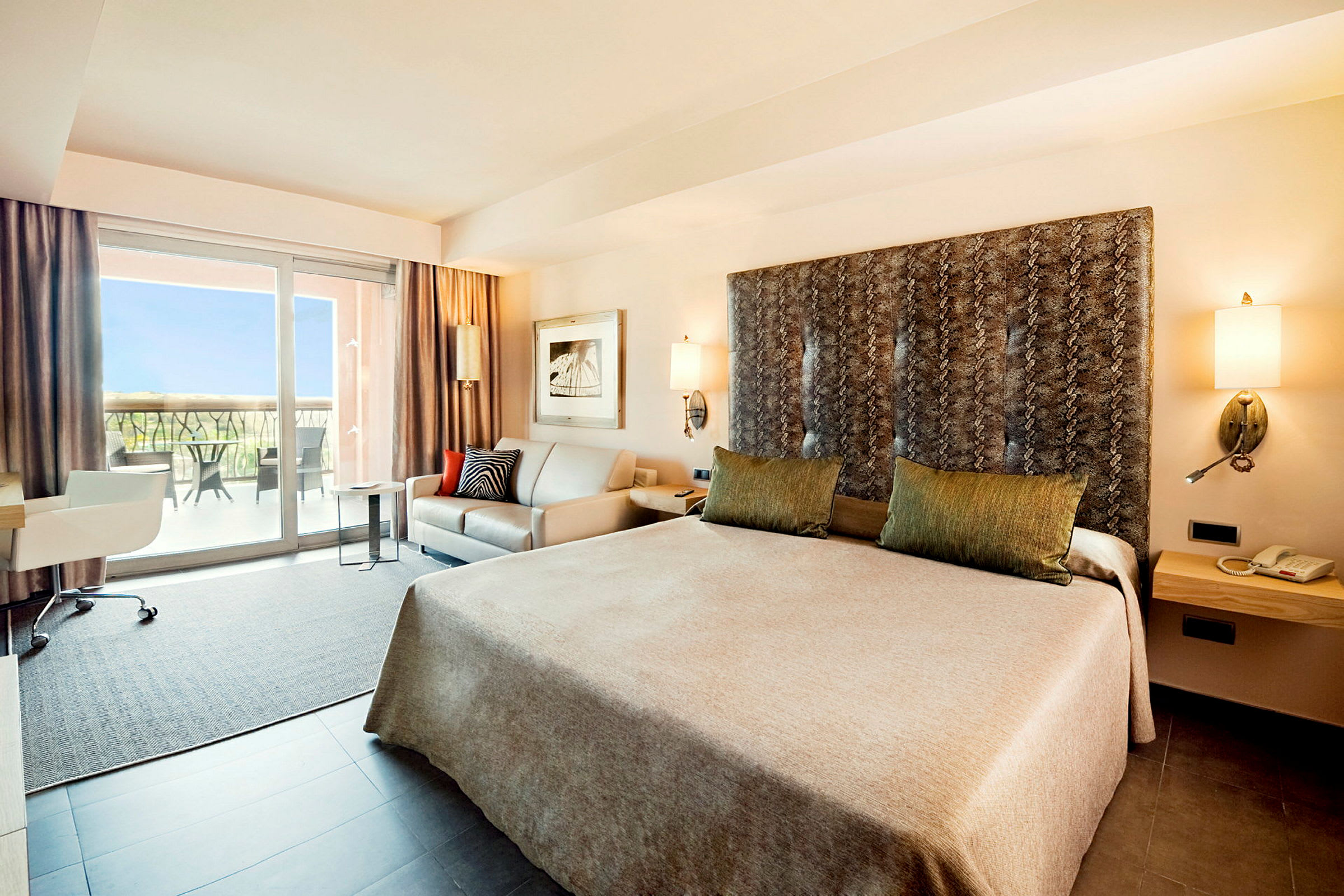 Ett hotellrum med en stor säng, soffa, skrivbord och ett fönster som leder till en balkong. (AI-genererad text)