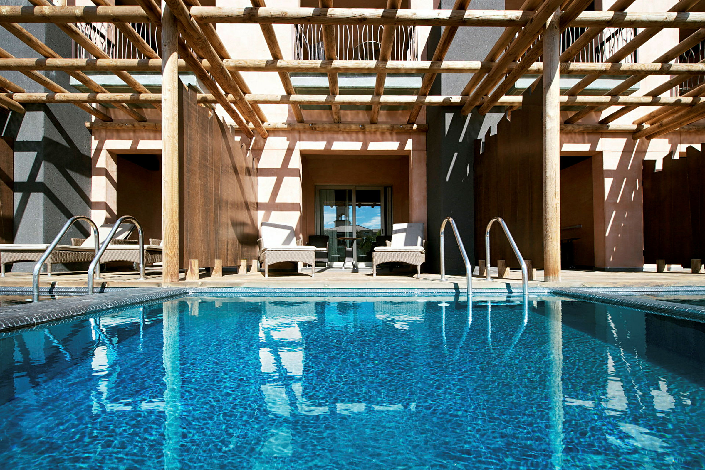En pool omgiven av sittmöbler och träpergola. (AI-genererad text)