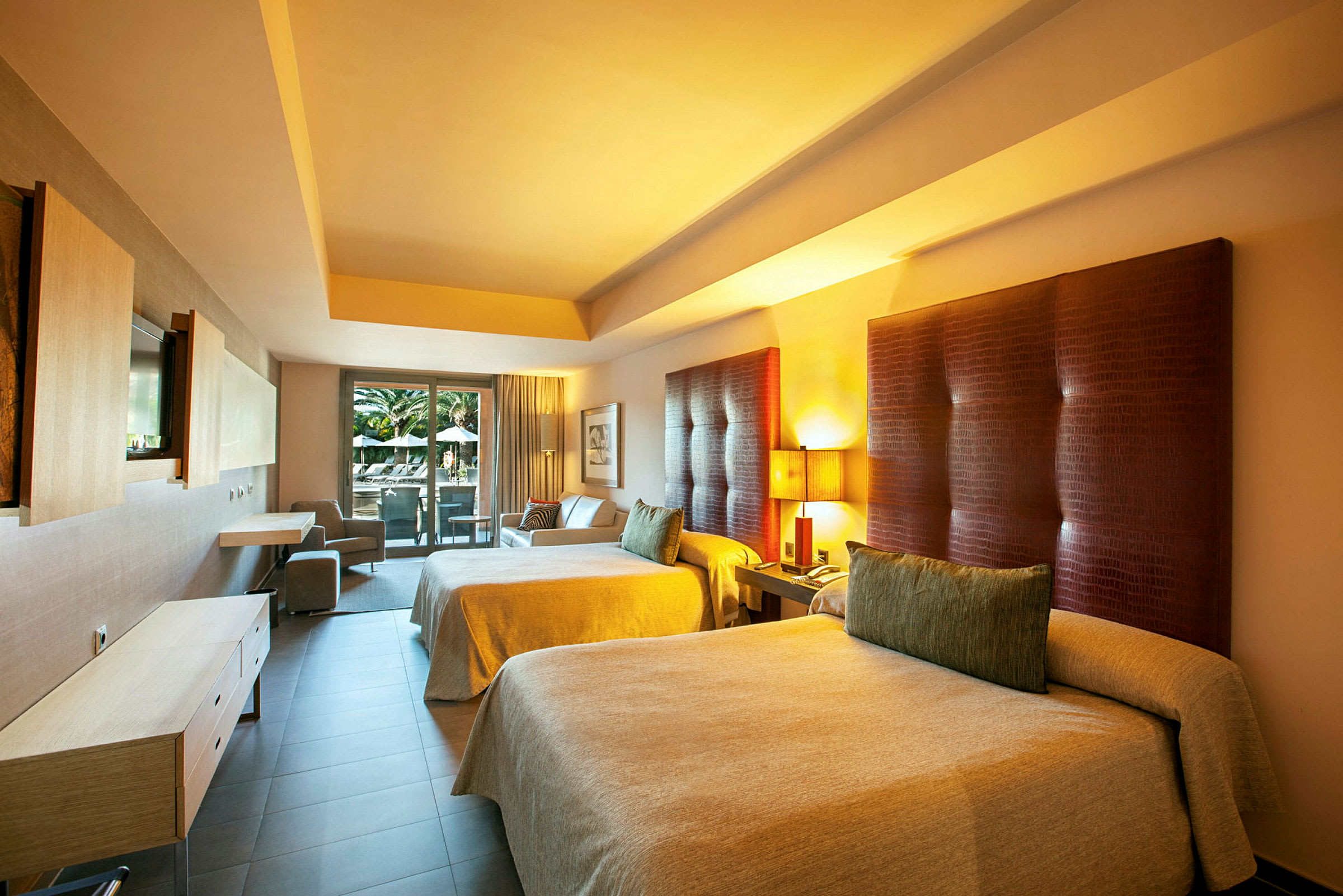 Ett hotellrum med två stora sängar, ett skrivbord, en soffa och en balkong med utsikt över en pool. (AI-genererad text)
