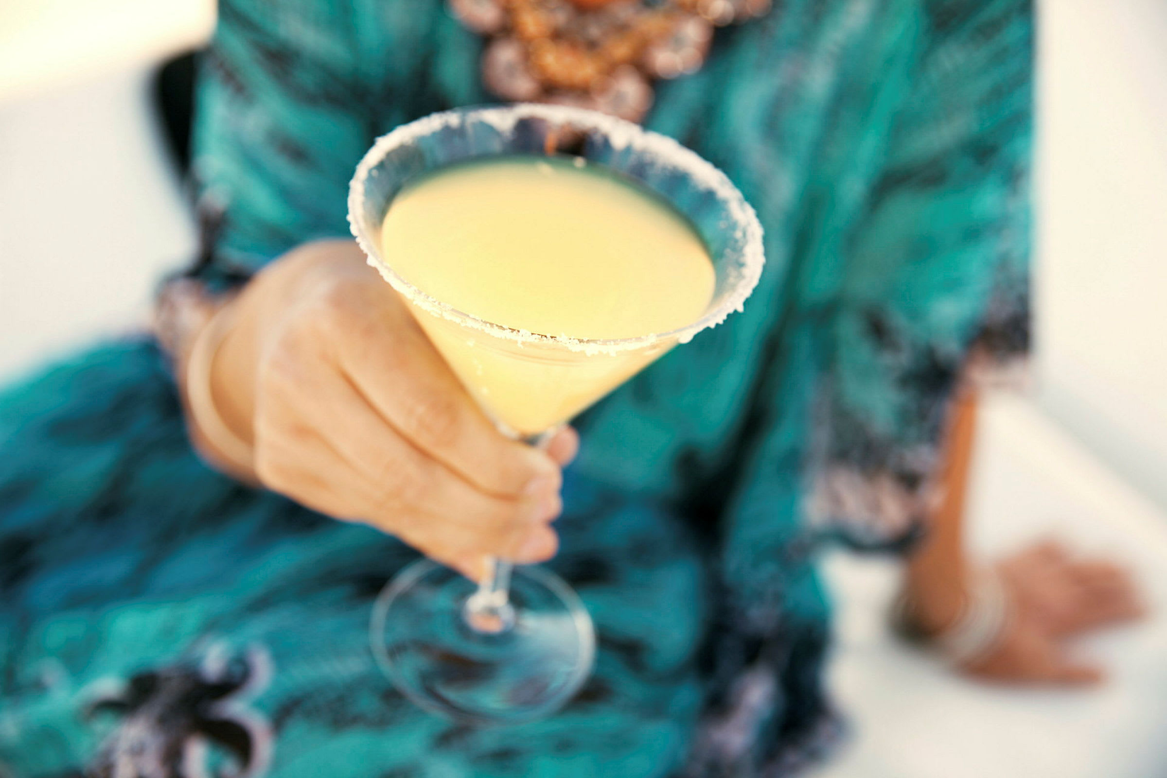 En person håller ett cocktailglas fyllt med gul dryck och dekorerat med en sockrad kant. (AI-genererad text)