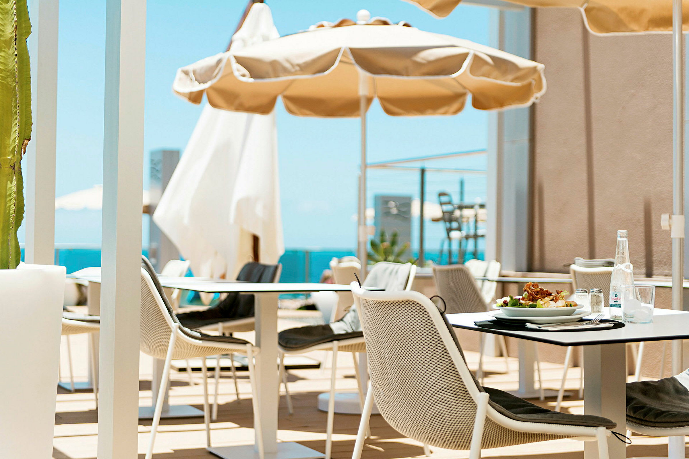 En utomhusrestaurang med parasoller och utsikt över havet. (AI-genererad text)