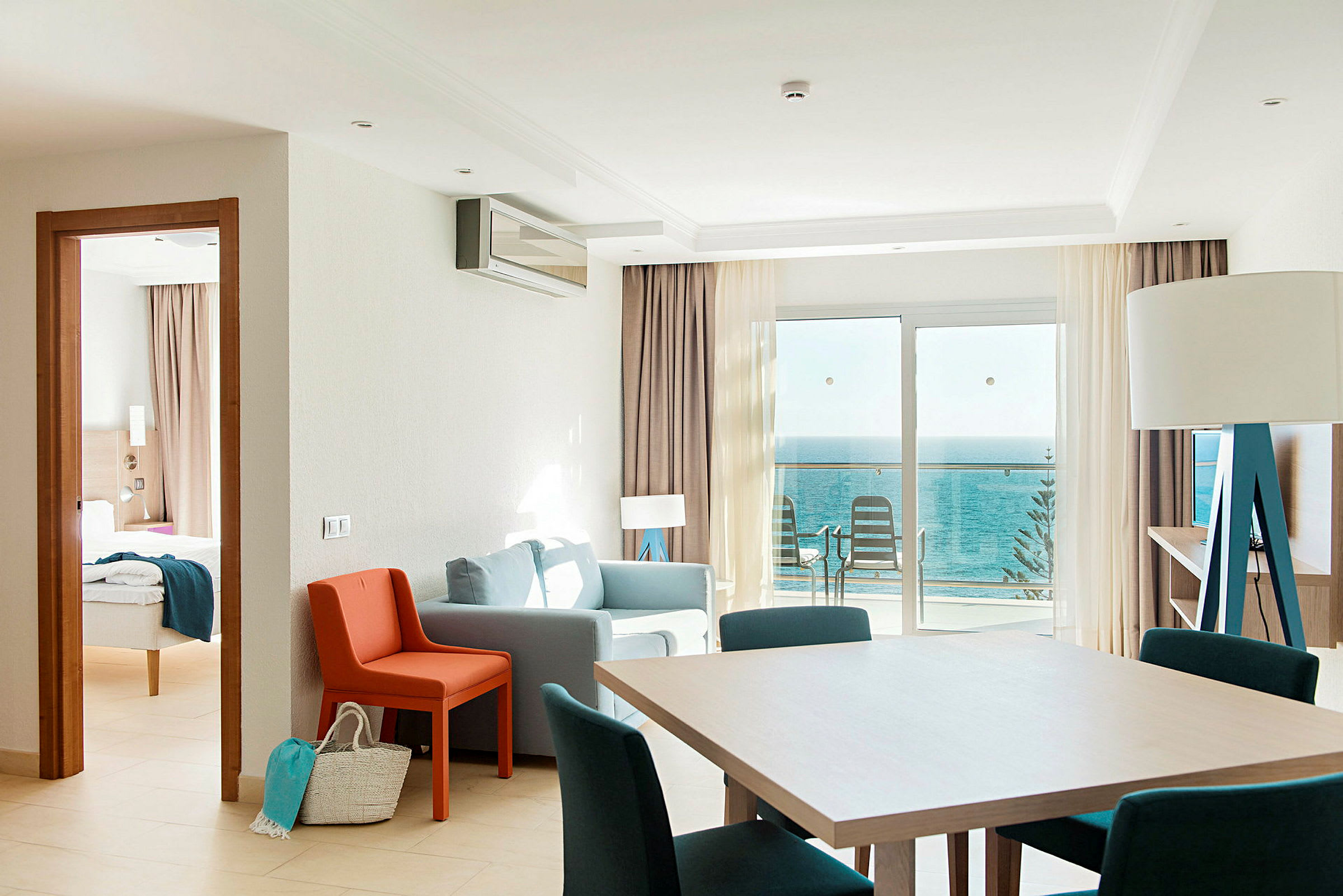 Ett hotellrum med sittgrupp, matbord och havsutsikt från balkongen. (AI-genererad text)