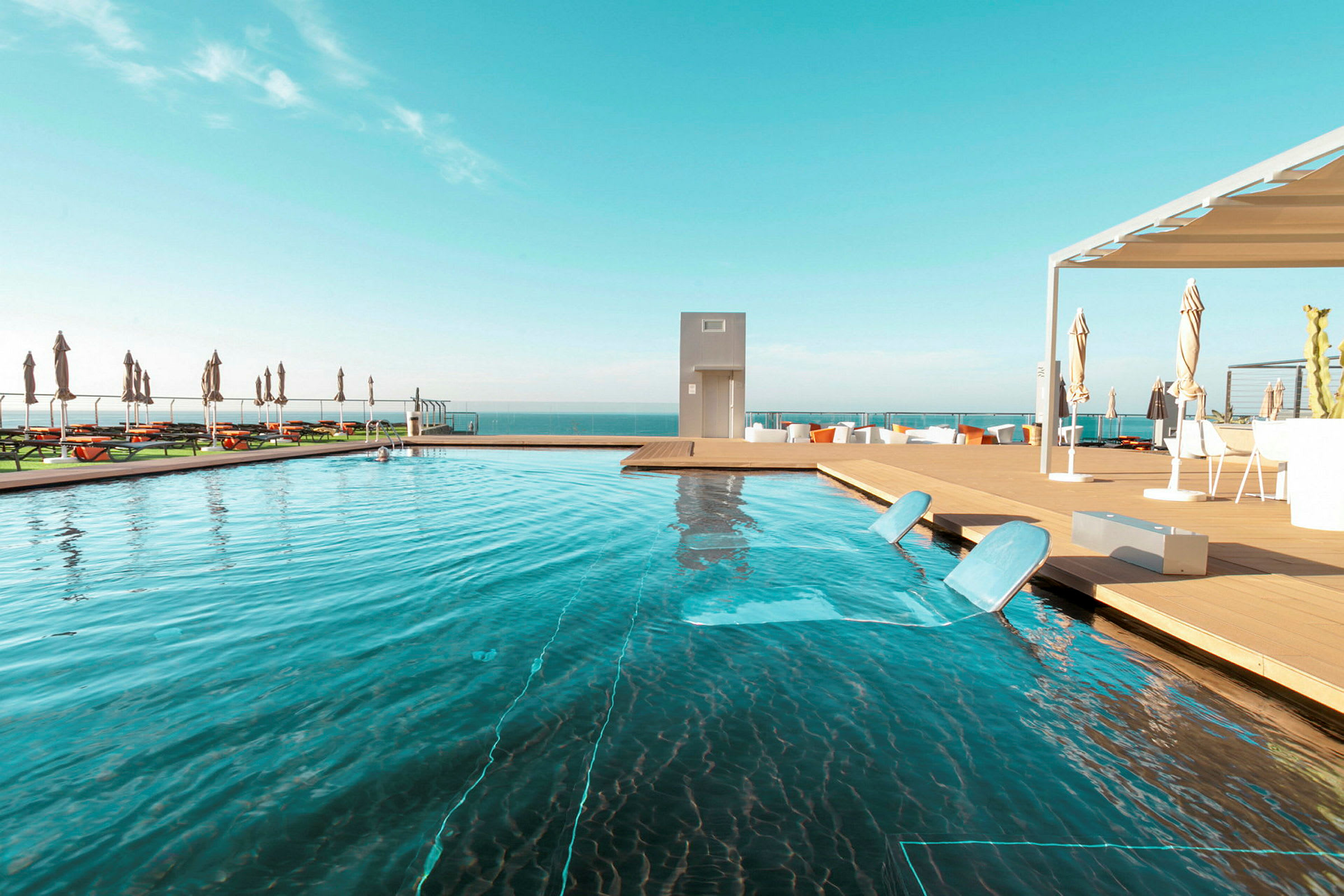 Utomhuspool med solstolar bredvid och havet i bakgrunden. (AI-genererad text)