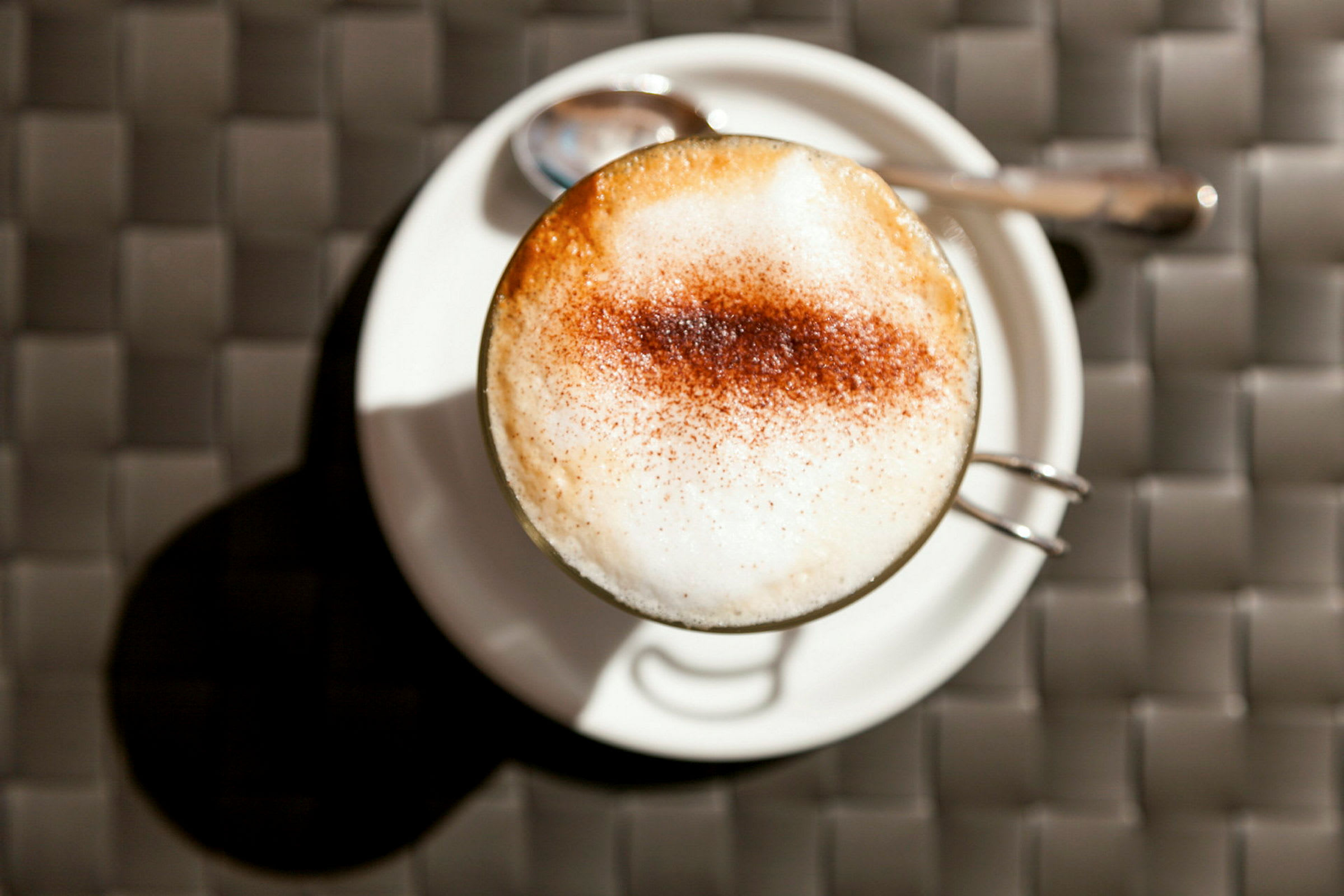 En kopp cappuccino på ett vitt fat med en sked bredvid. (AI-genererad text)