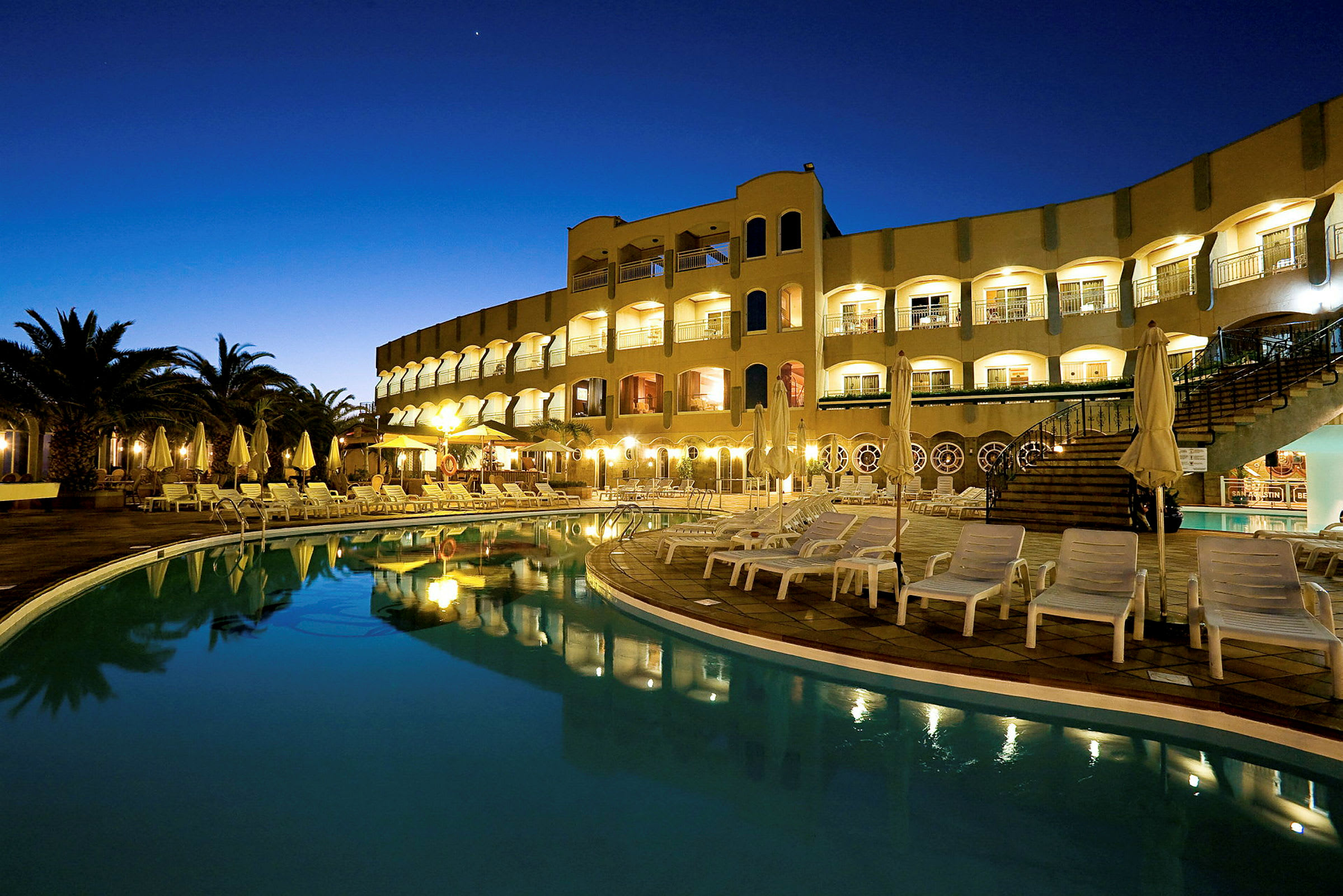 Ett hotell med en pool och solstolar vid skymning. (AI-genererad text)