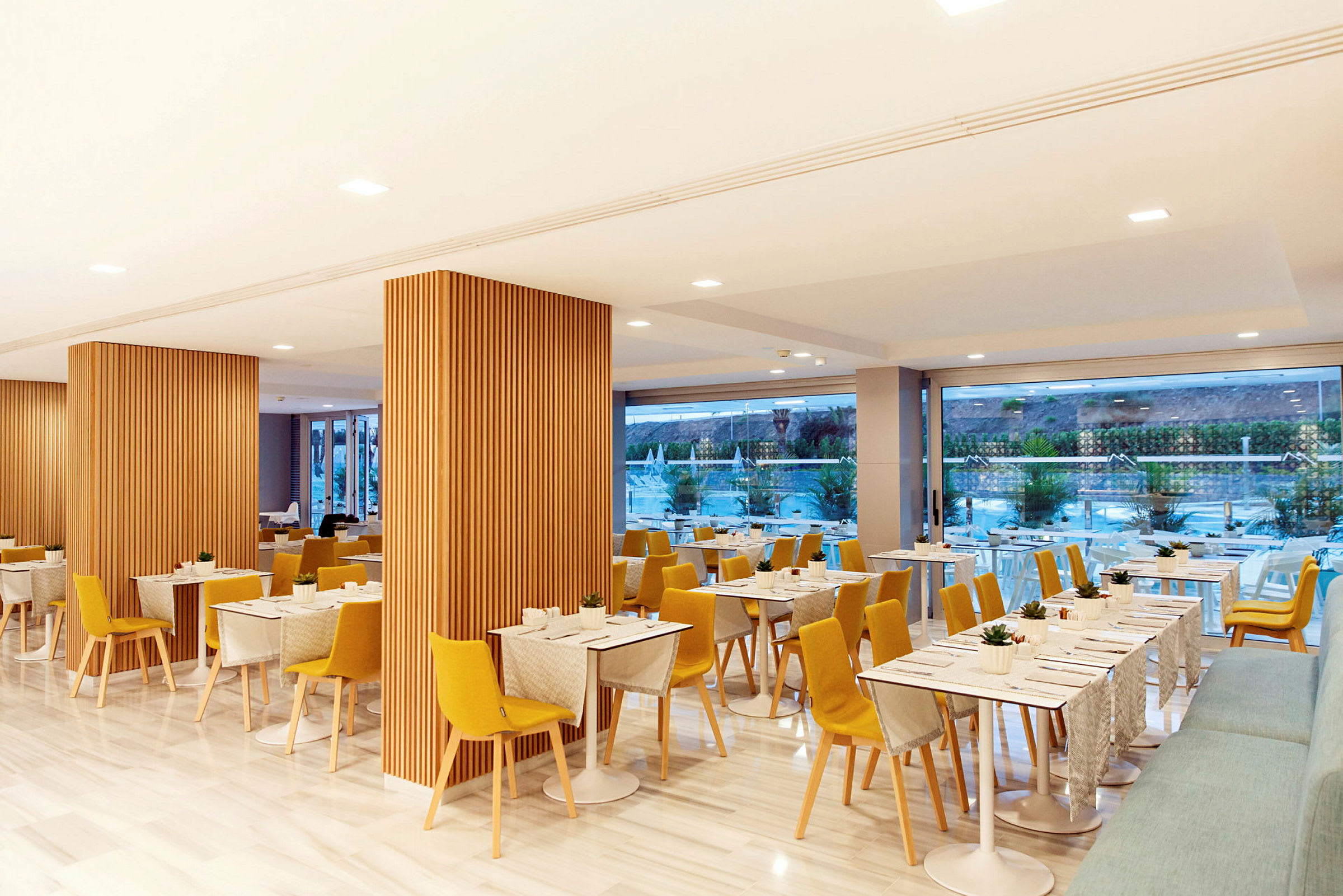 Bild av en modern restaurang med trädekorationer, gula stolar och bord med dukar. (AI-genererad text)
