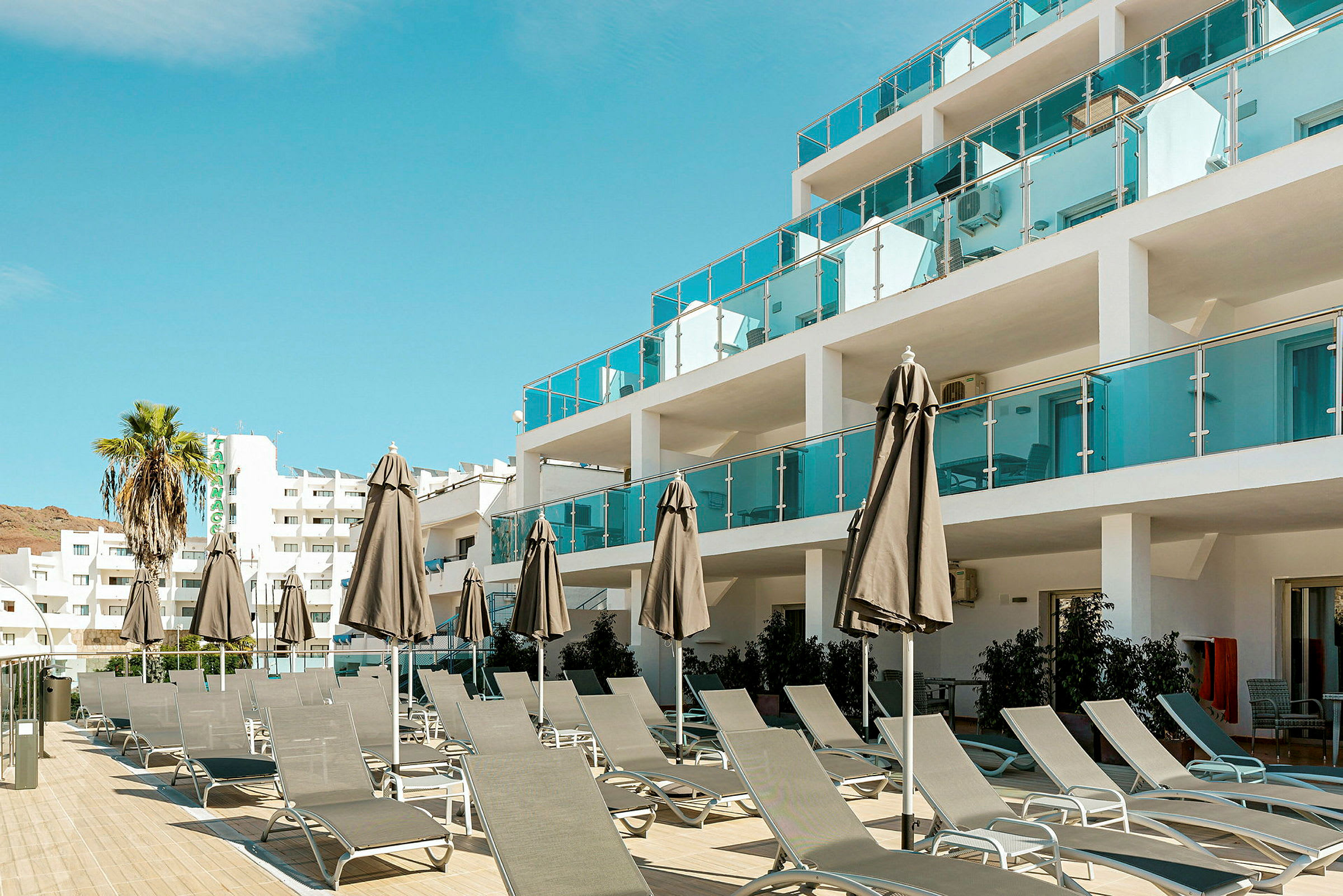 Bild av en hotellbyggnad med solstolar och parasoller vid en uteplats. (AI-genererad text)