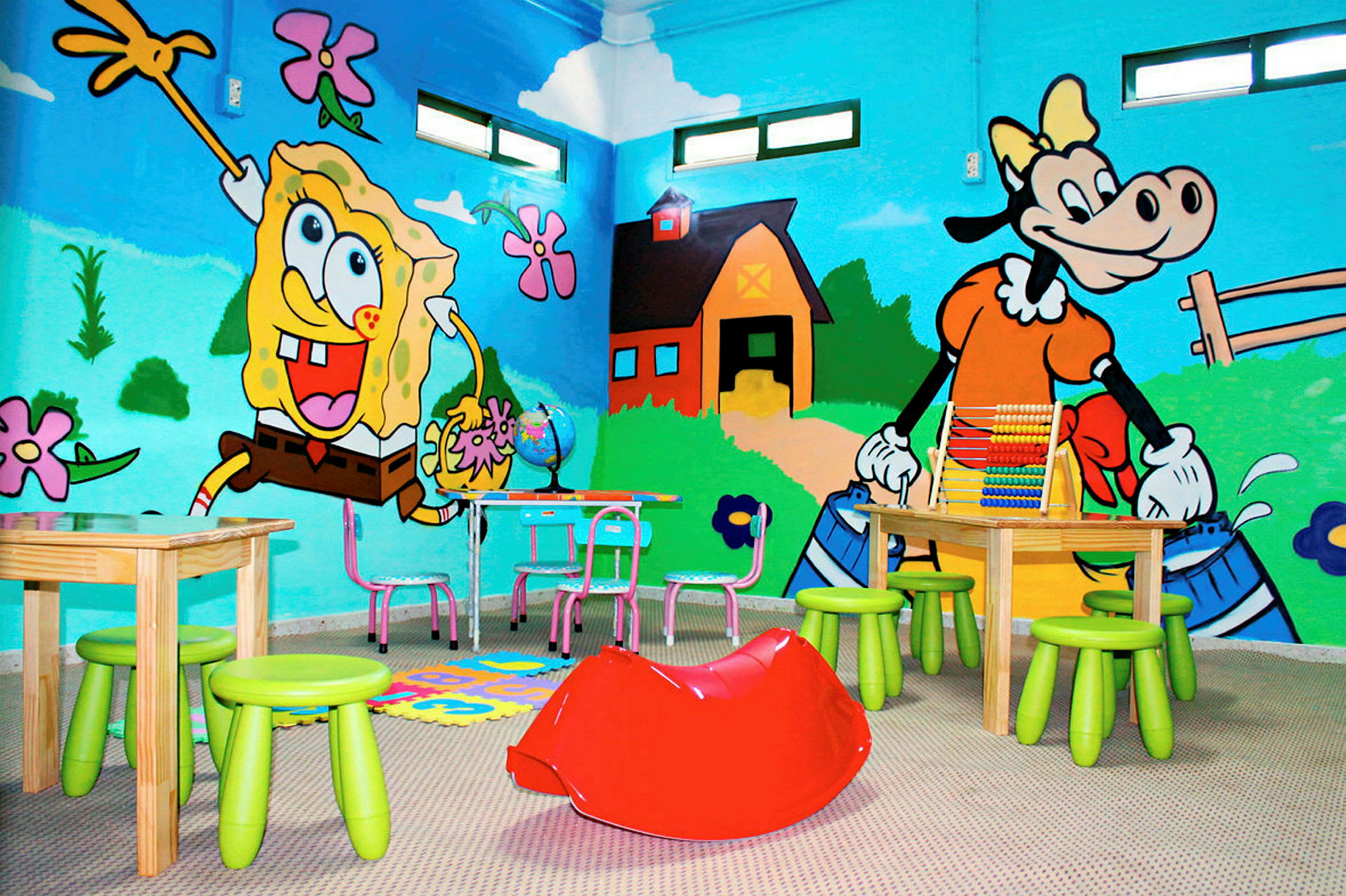 Ett rum med barnmöbler och färgglada väggmålningar av Spongebob och en kofigur. (AI-genererad text)