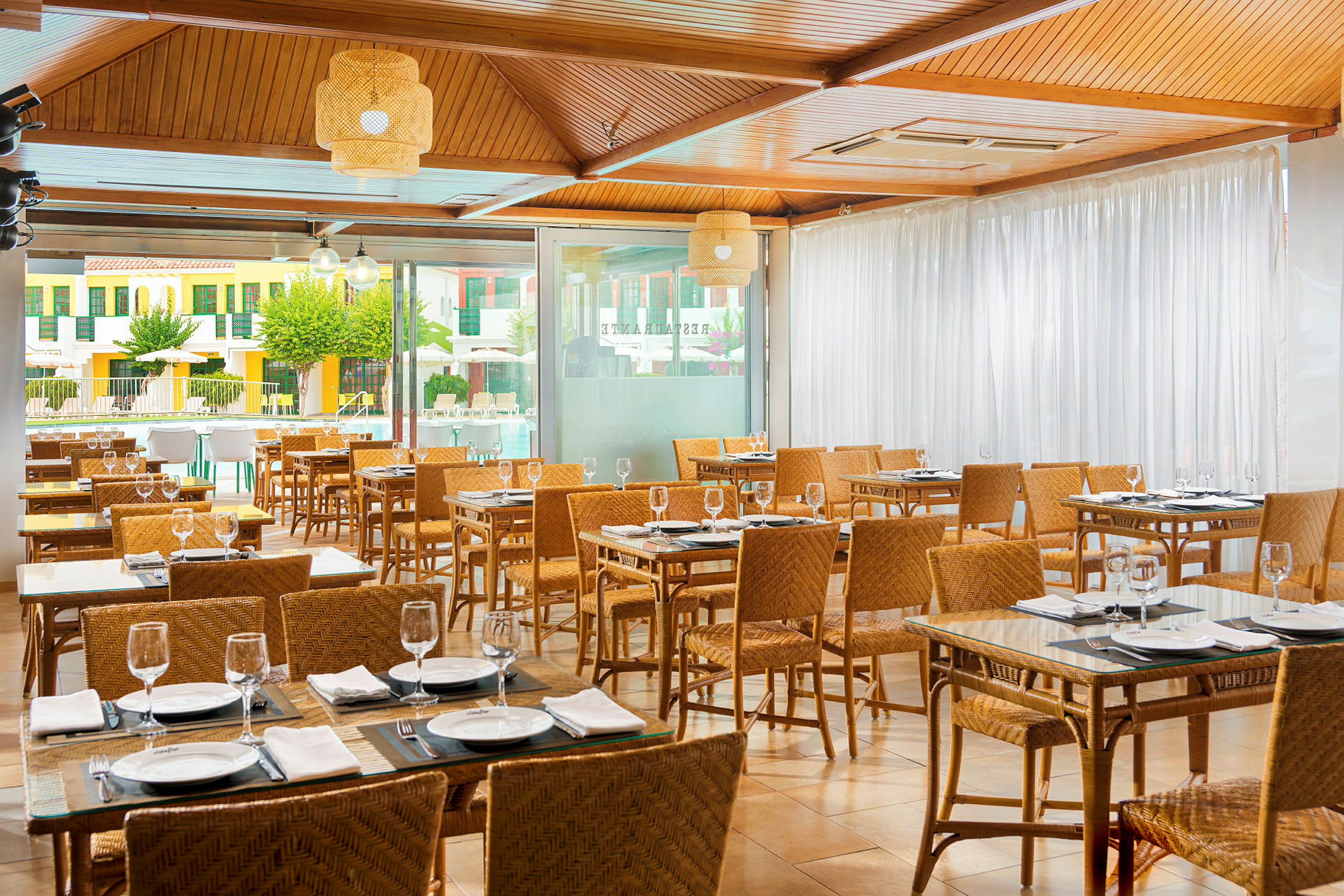 Innerrestaurang med dukade bord och rottingstolar. (AI-genererad text)