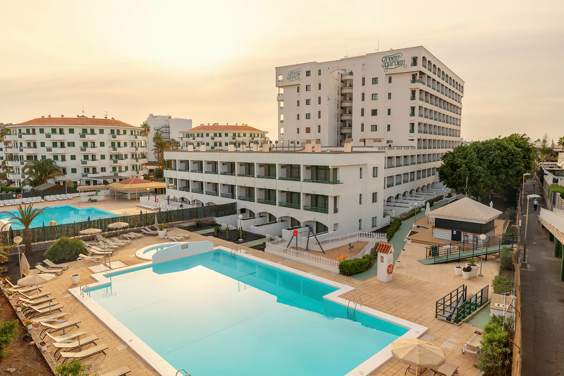Ett hotellkomplex med flera byggnader, två pooler och solstolar. (AI-genererad text)