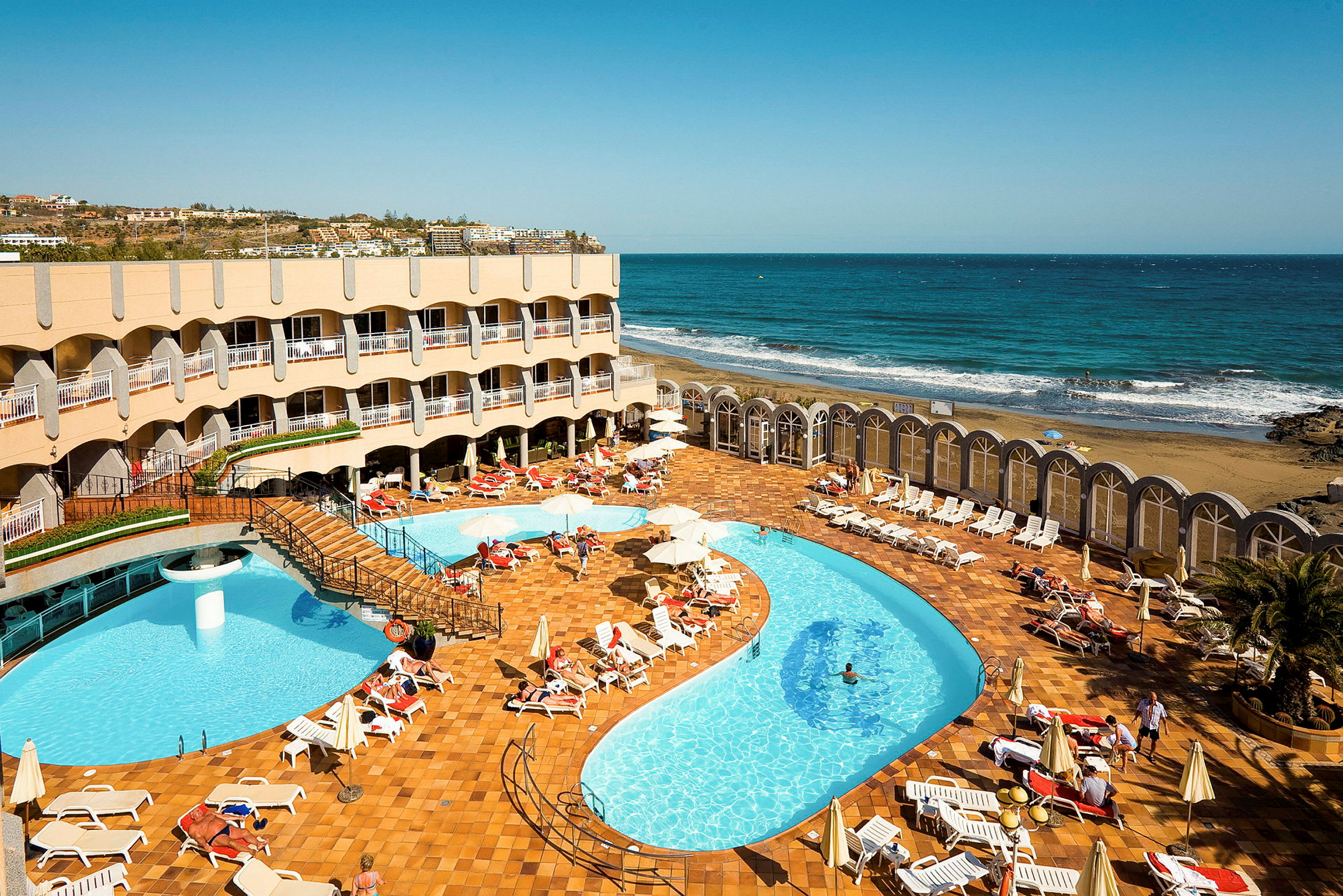 Hotellområde med pool och solstolar nära havet. (AI-genererad text)
