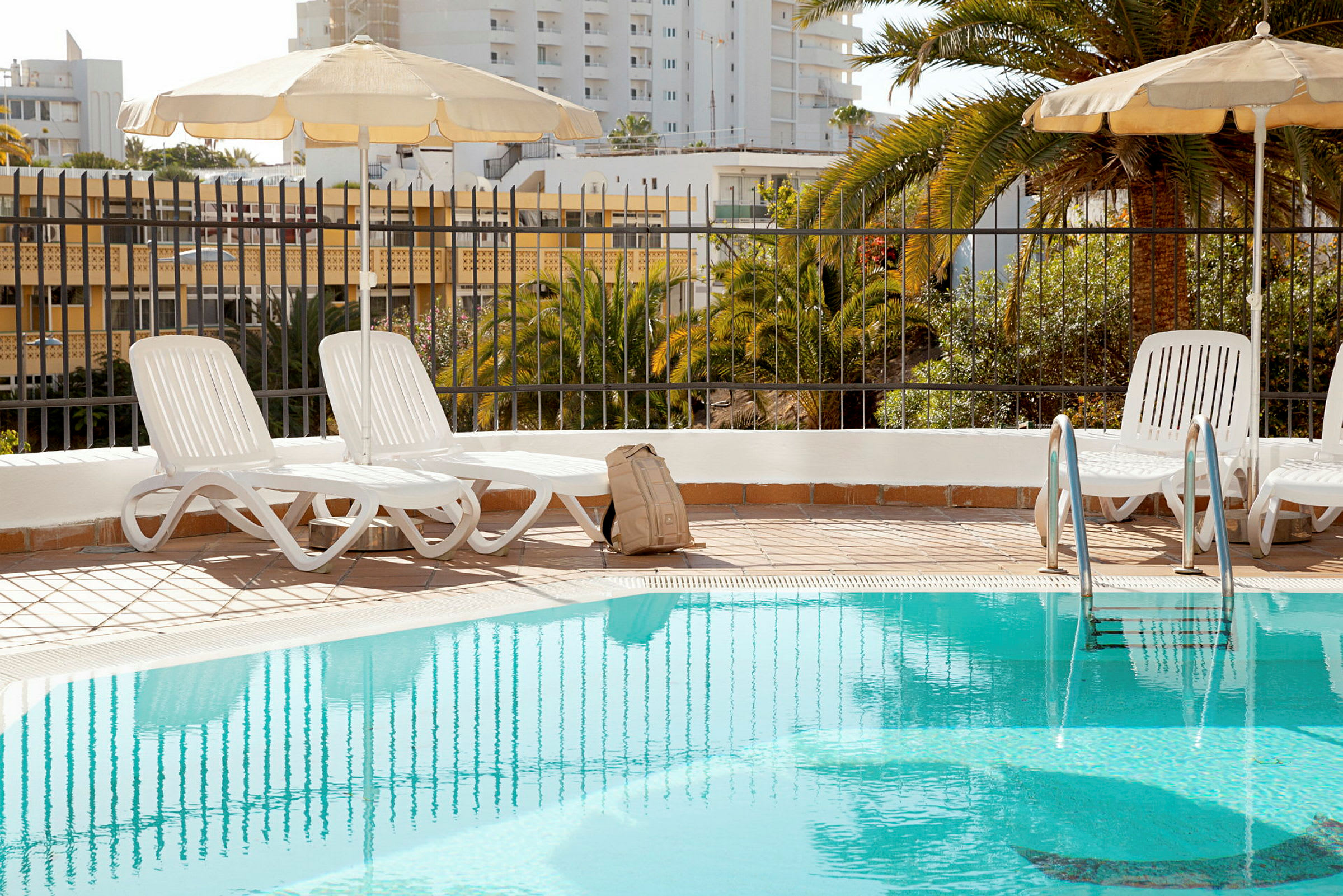 Solstolar och paraplyer vid en pool med en ryggsäck placerad på marken. (AI-genererad text)
