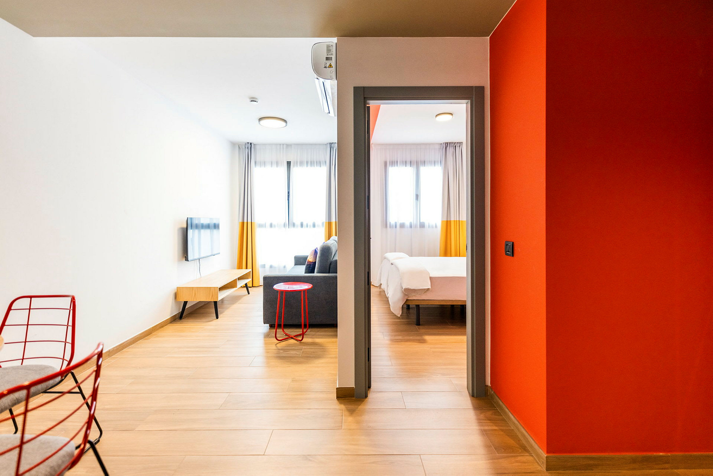 Ett modernt hotellrum med trägolv och inbjudande inredning. Rummet har en sittgrupp med soffa, väggmonterad TV och ett sovrum med en dubbelsäng. (AI-genererad text)