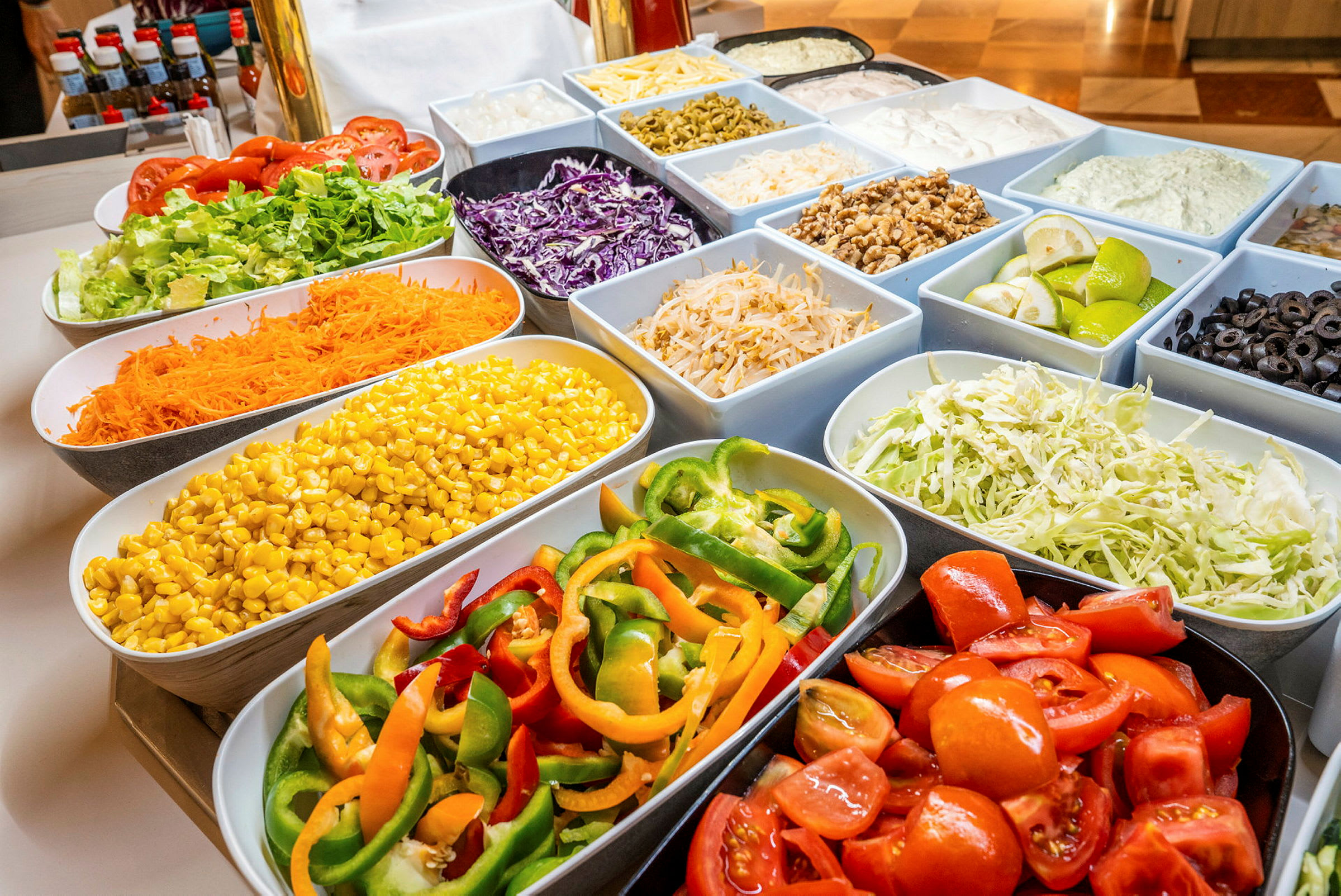 Ett buffébord fullt av olika grönsaker i skålar, inklusive tomater, sallad, majs, paprika och oliver. (AI-genererad text)