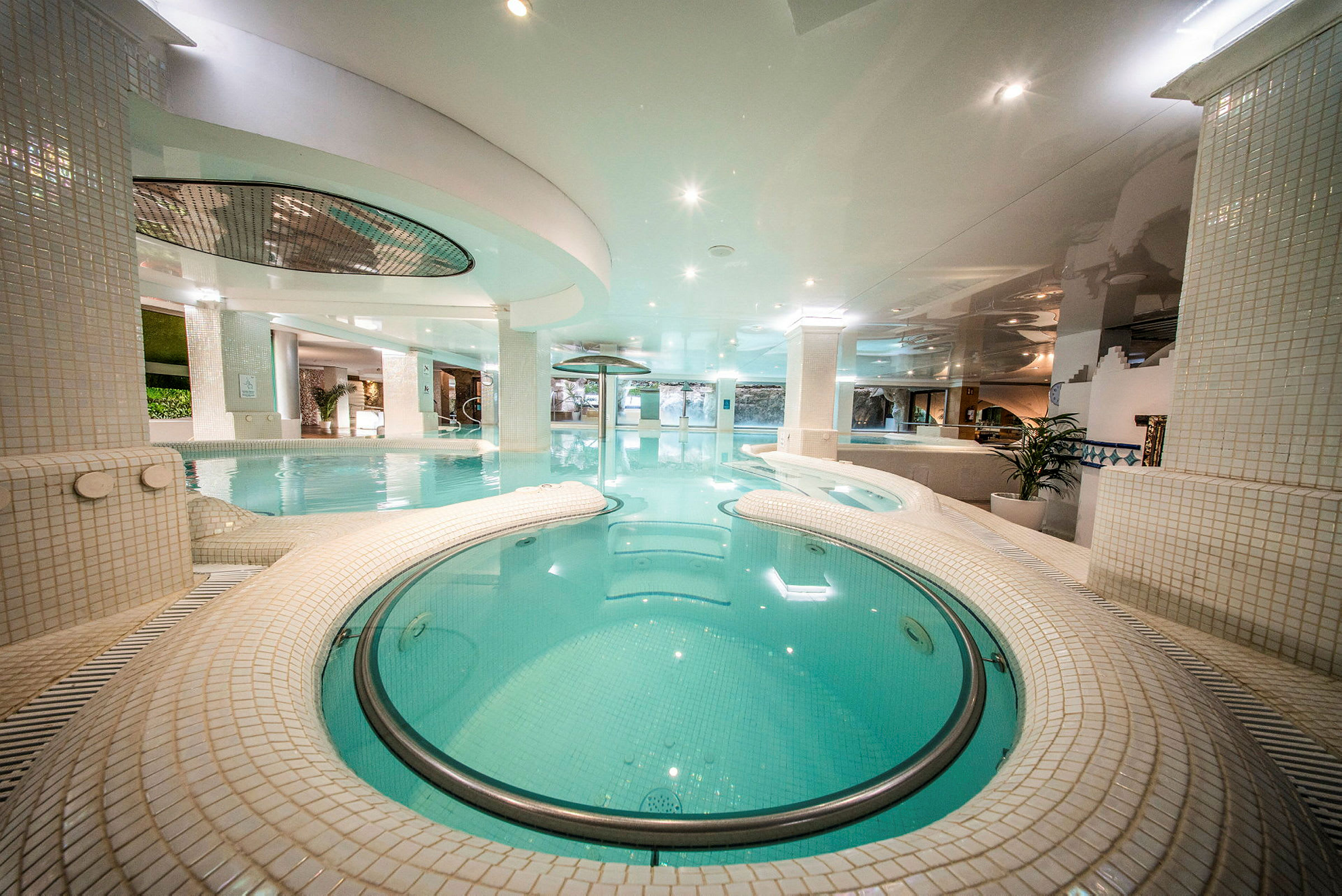 En inomhuspool med en modern design, omgiven av ljus kakel och belysning. (AI-genererad text)