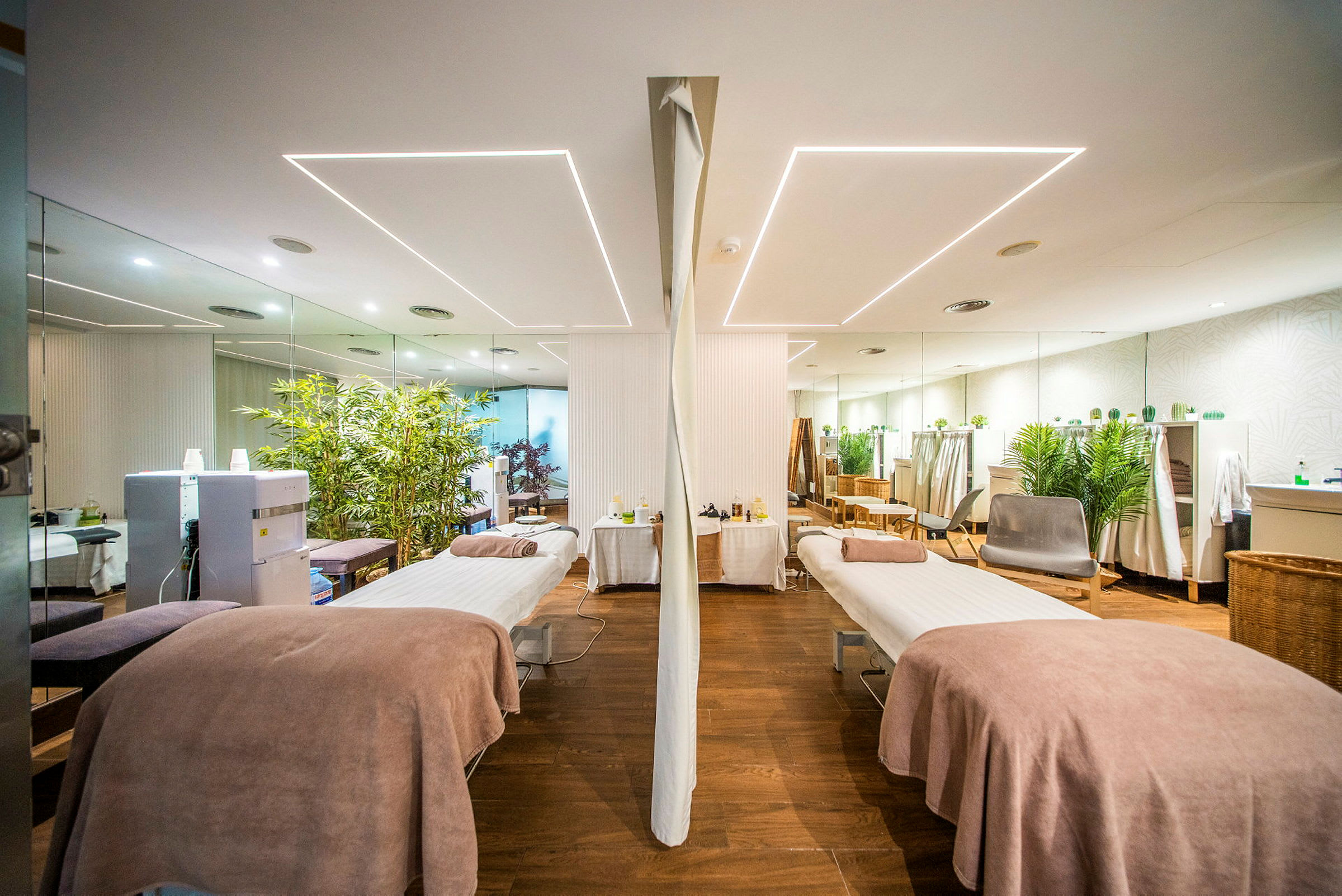 Ett spa-rum med två massagebänkar, inrett med växter och speglar. (AI-genererad text)