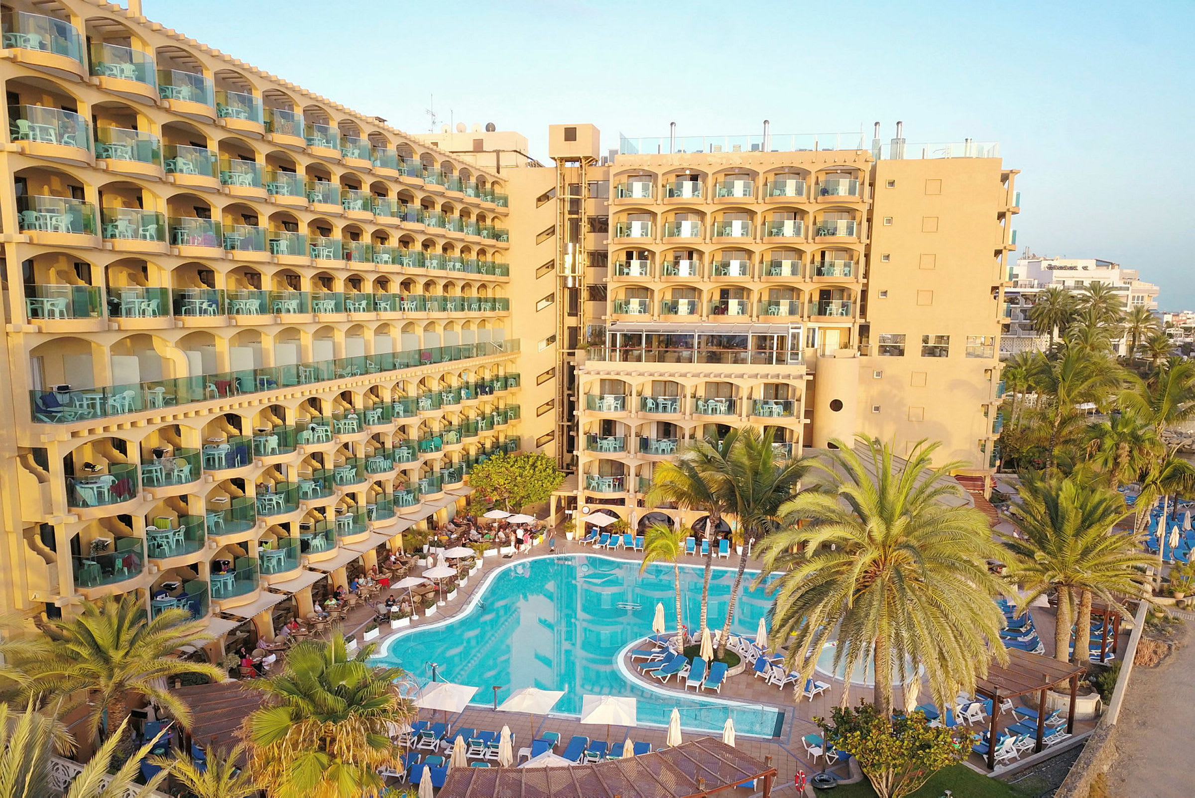 Hotell med gul fasad, balkonger och swimmingpool. (AI-genererad text)