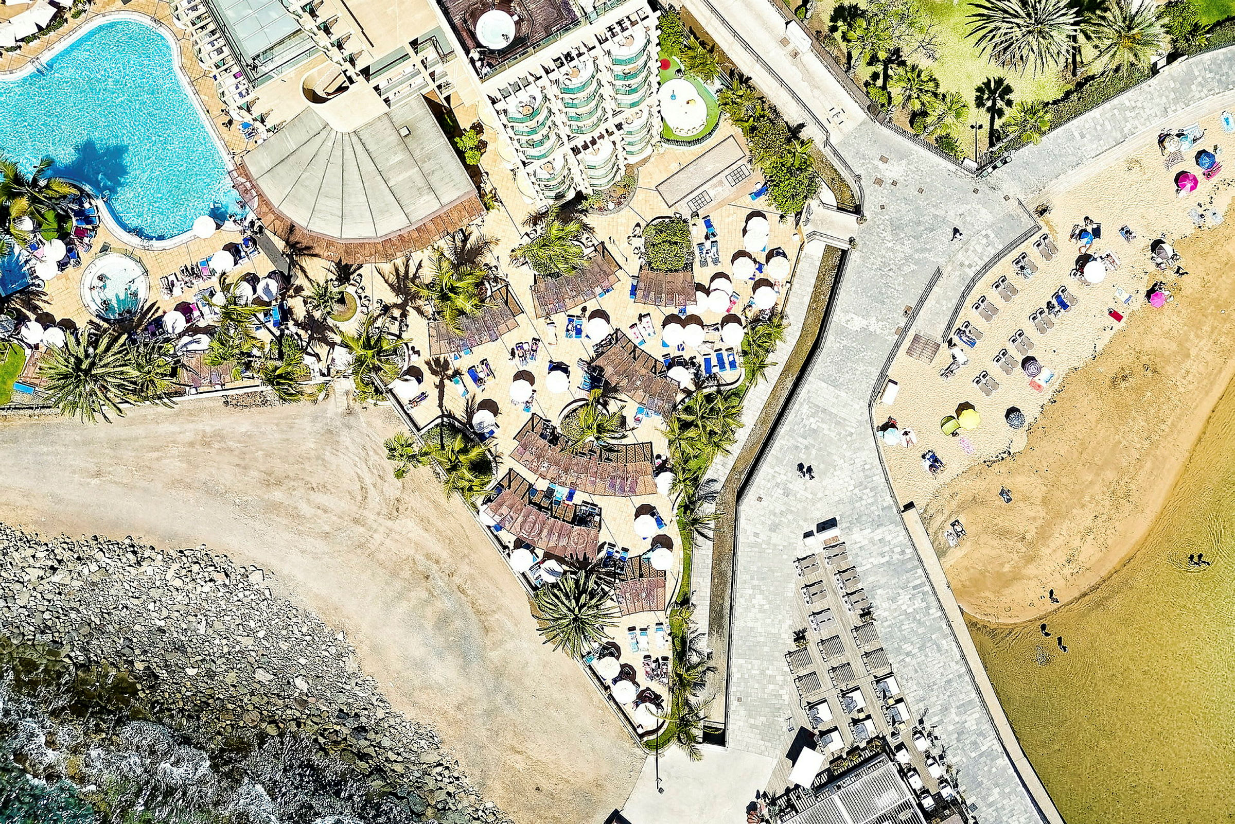 Flygbild på en badort med swimmingpooler, solstolar och parasoller nära stranden. (AI-genererad text)