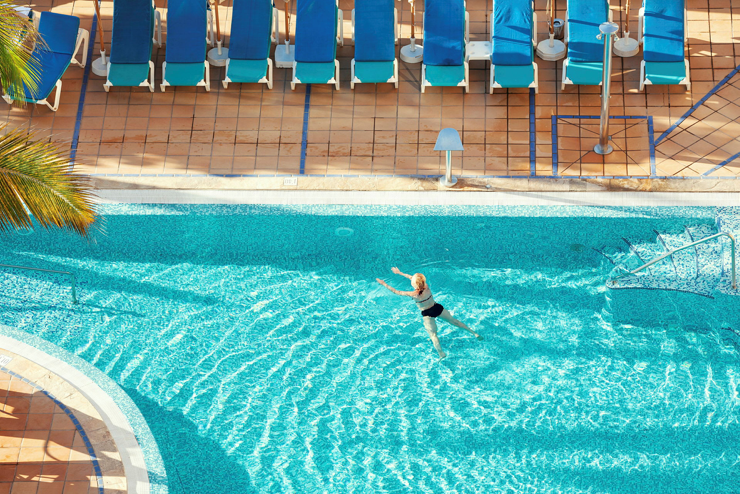 En person simmar i en pool nära flera solstolar. (AI-genererad text)