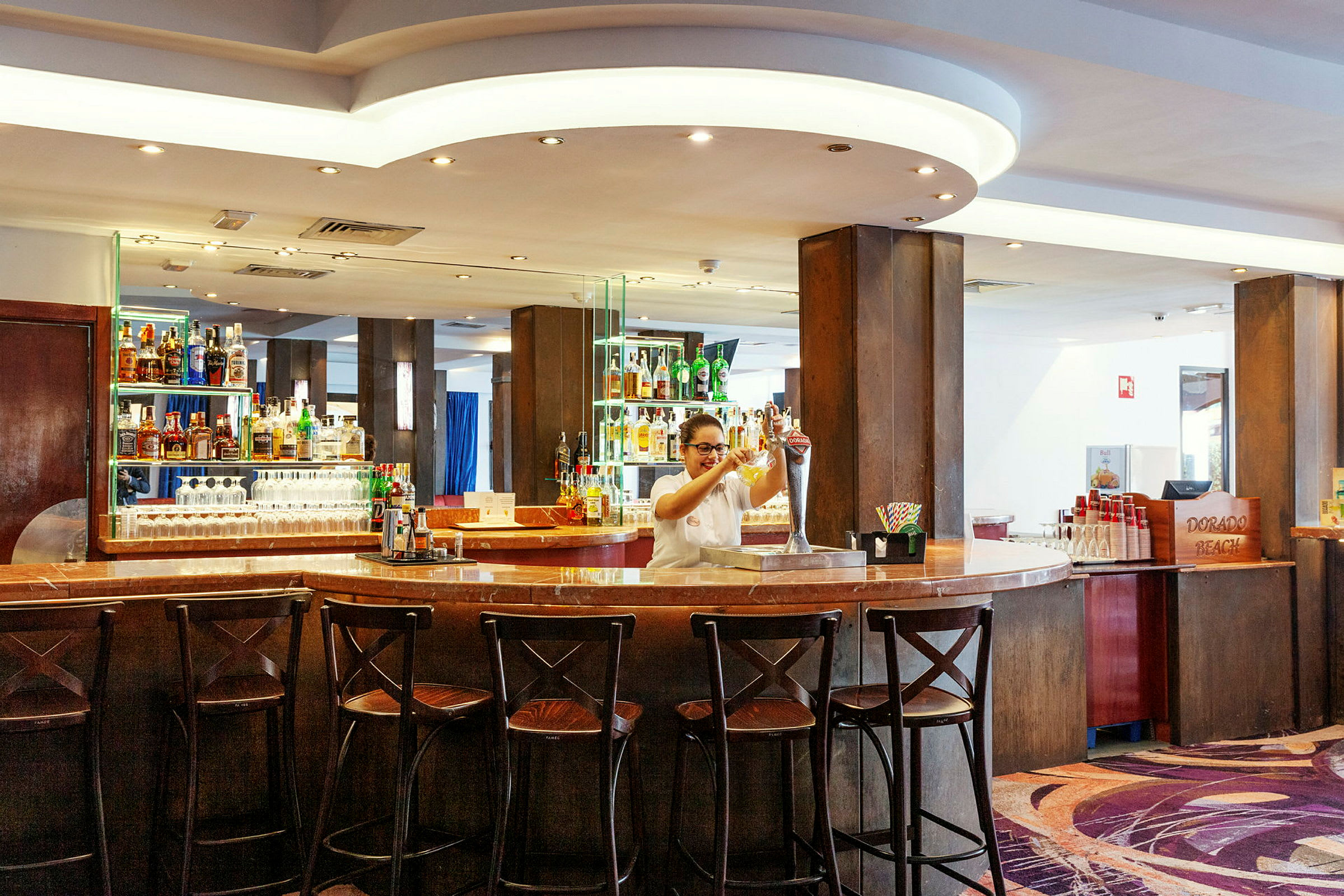 Bilden visar en välupplyst hotellbar med mörk träinredning och flera stolar vid bardisken. (AI-genererad text)