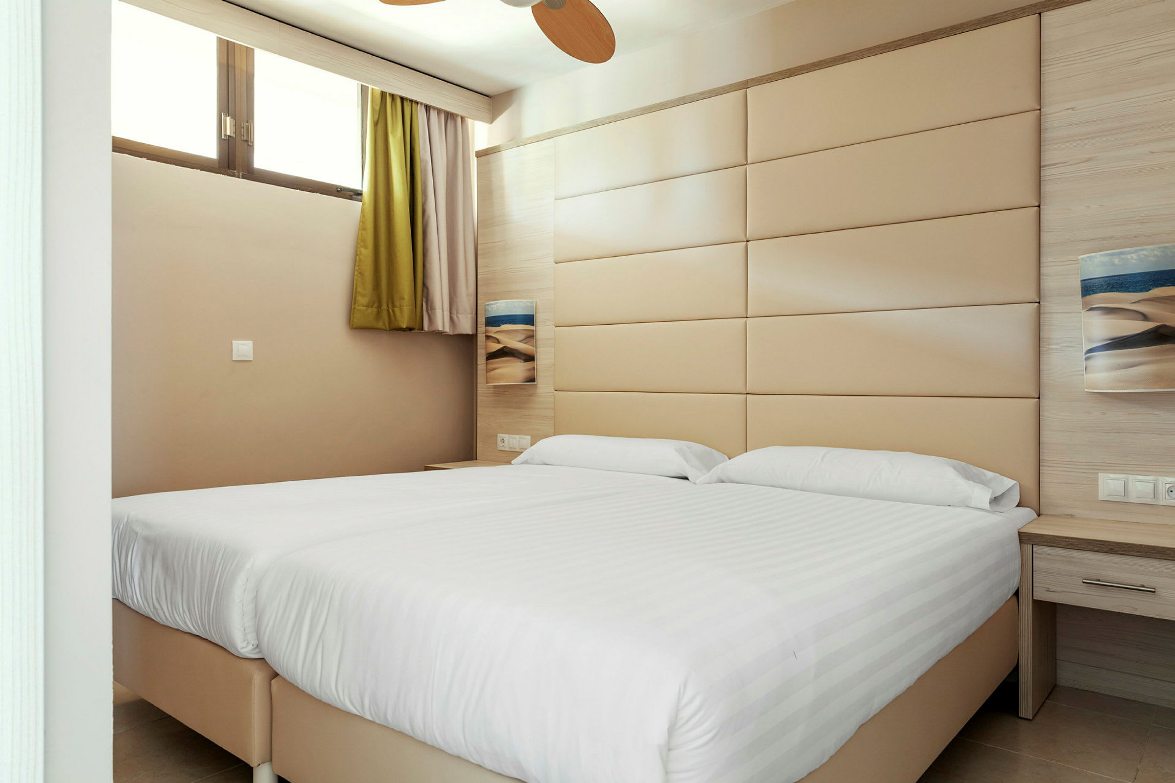 Ett hotellrum med två sängar och en beige väggpanel. (AI-genererad text)