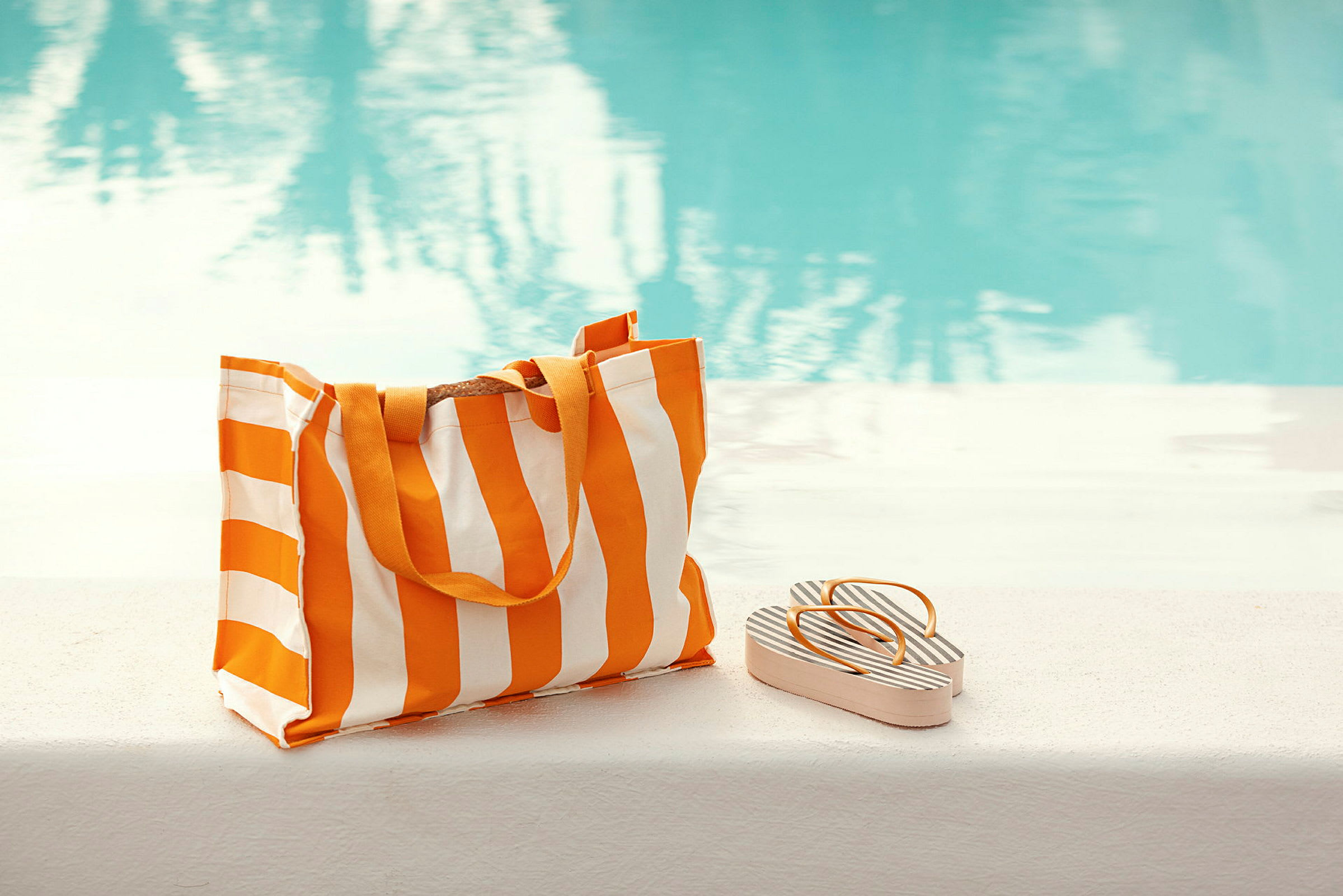 En randig strandväska och sandaler ligger bredvid en pool. (AI-genererad text)