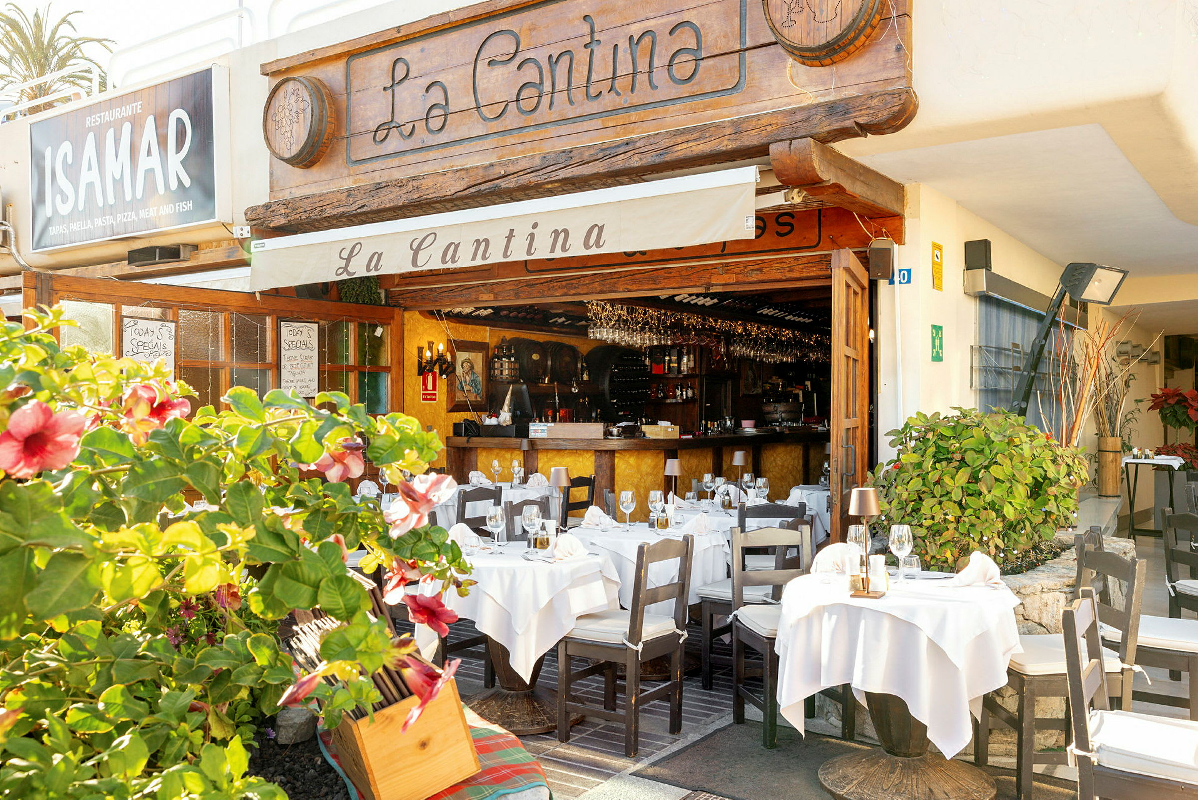 En restaurang med uteservering dekorerad med vita dukar och blomstrande växter. (AI-genererad text)