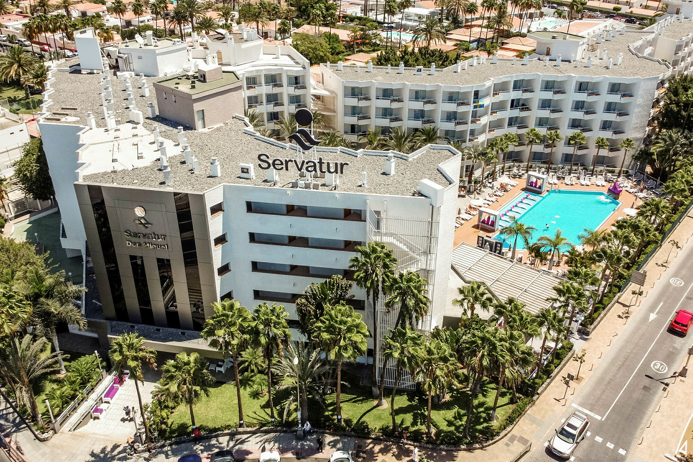 Luftvy av hotellbyggnad med poolområde och omgivande grönska. (AI-genererad text)