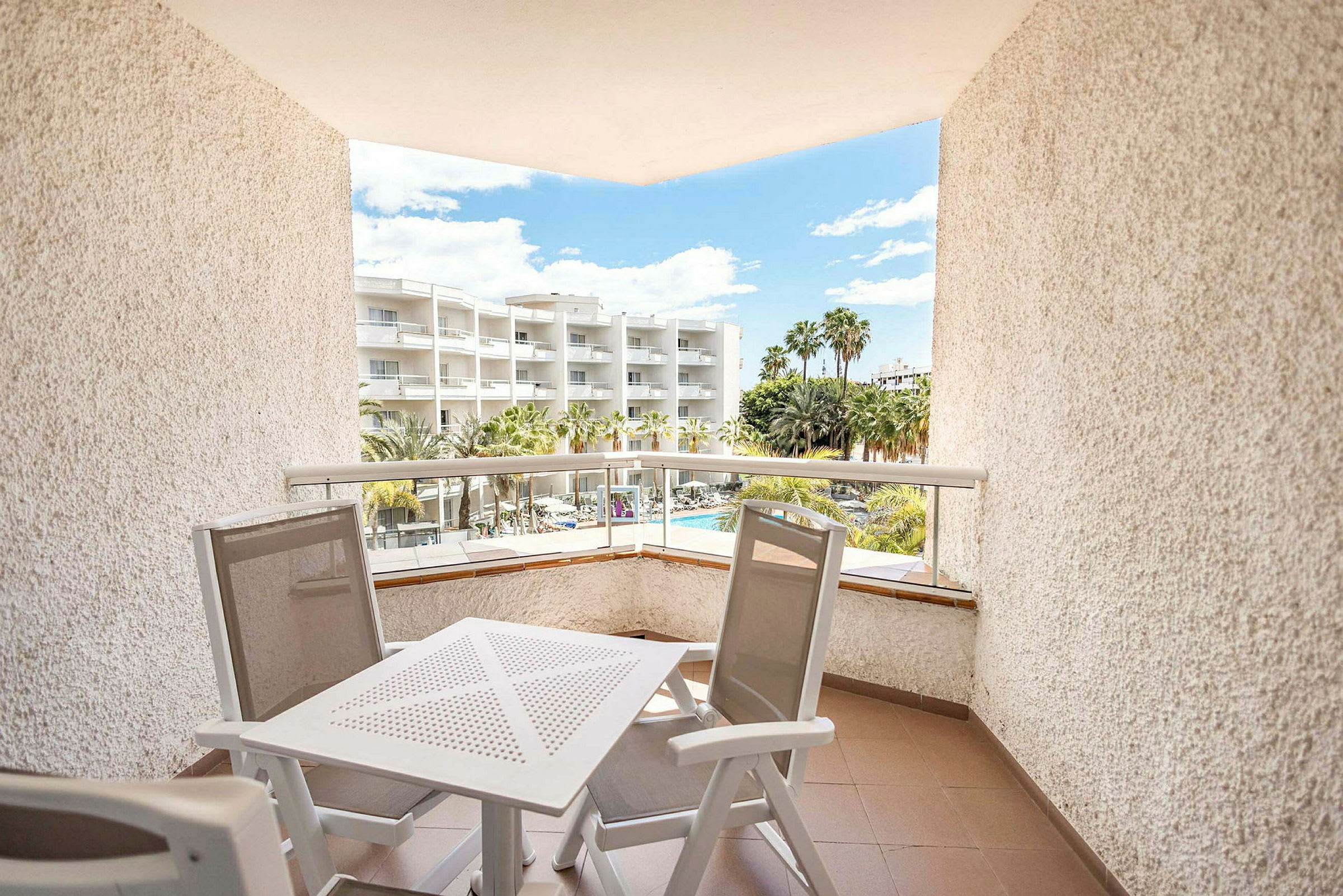 En balkong med utemöbler, utsikt över ett hotell med palmer och pool. (AI-genererad text)