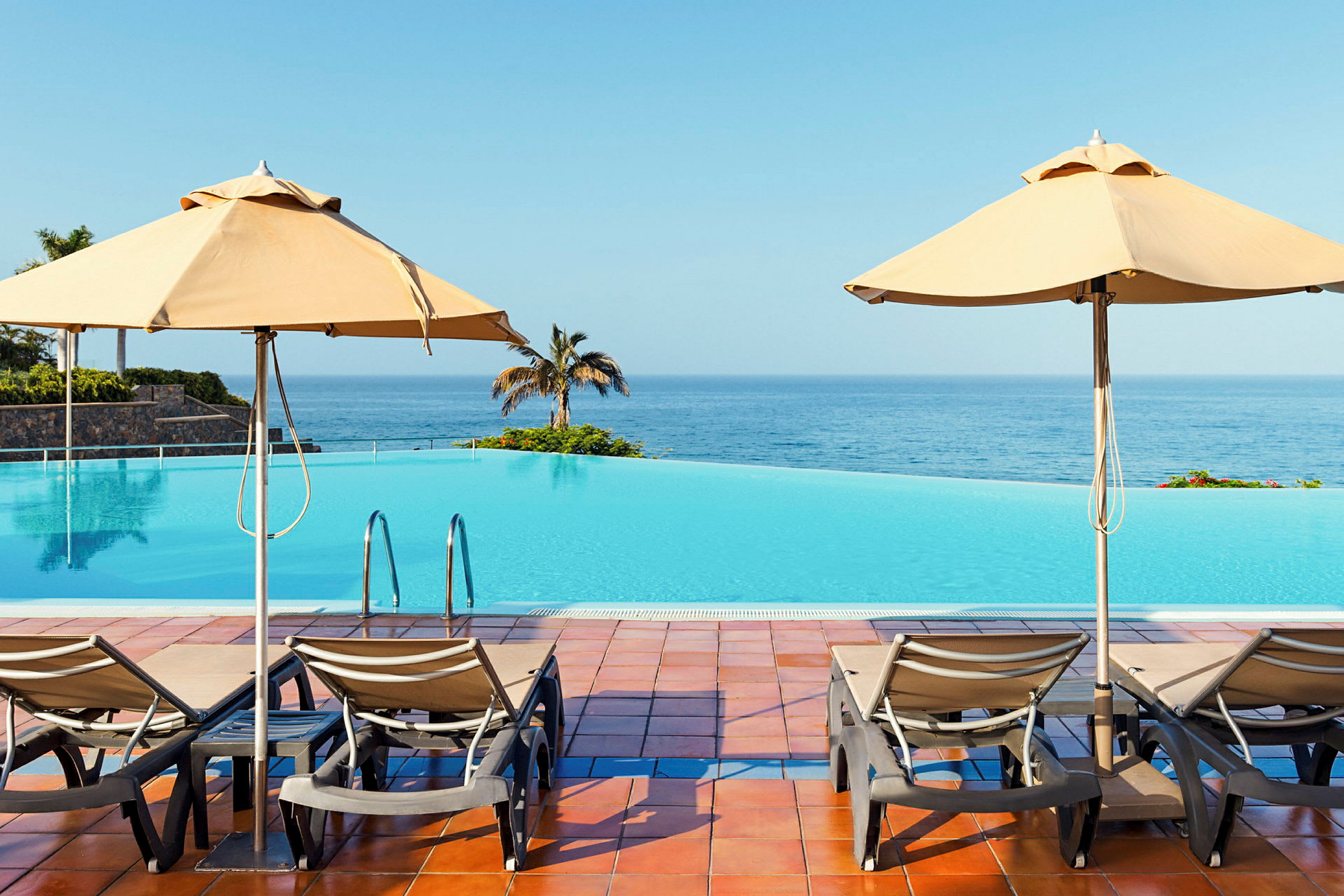 Två solstolar och parasoller vid en infinitypool med utsikt över havet. (AI-genererad text)