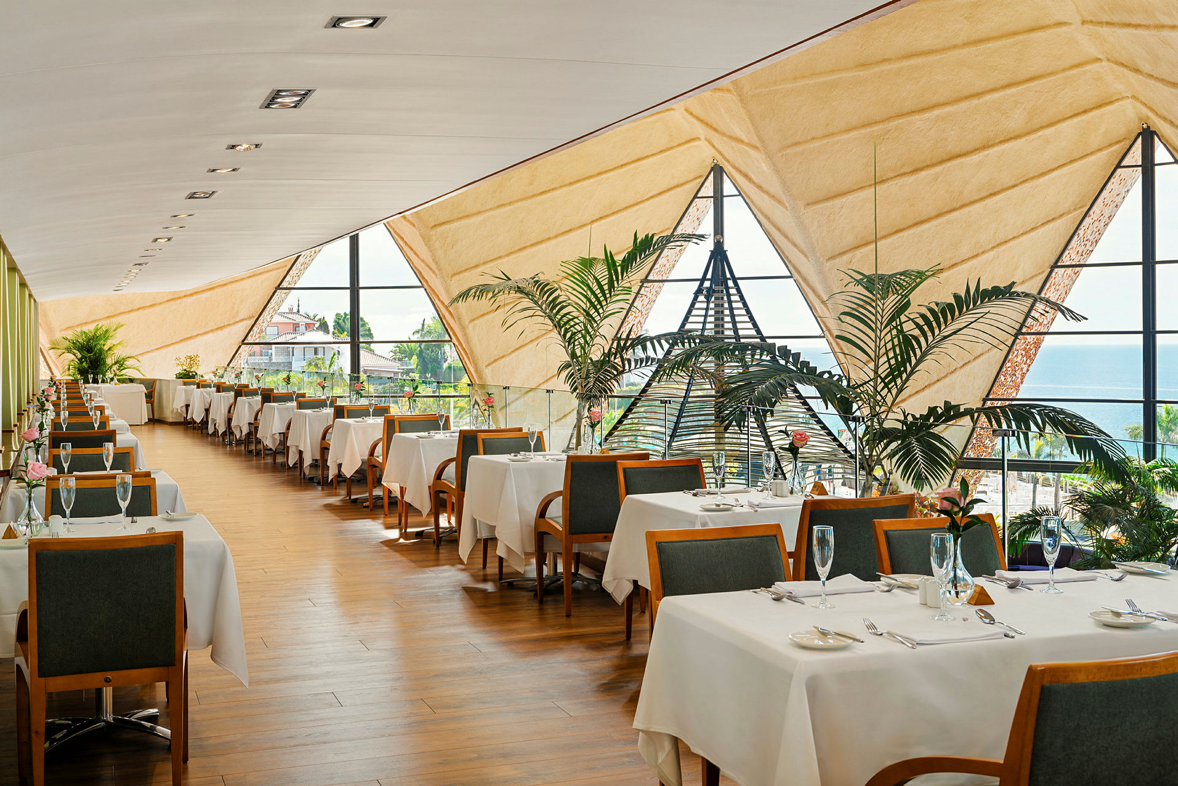 En elegant restaurang med bord täckta av vita dukar, stora fönster och grönskande växter. (AI-genererad text)