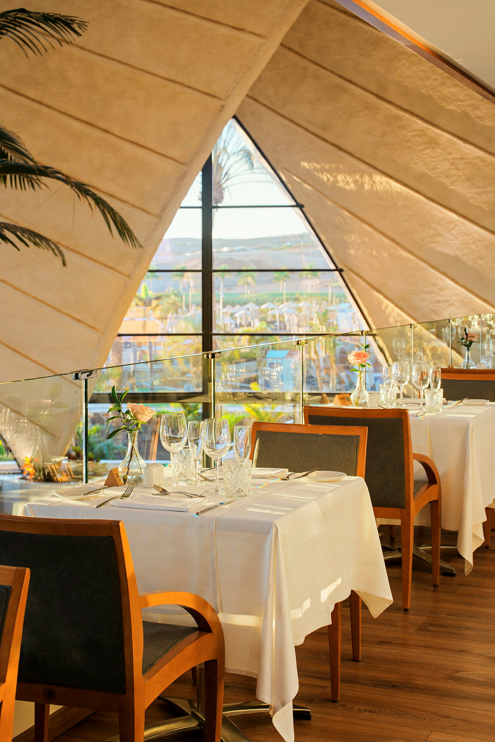 Restaurang med dukat bord intill ett stort fönster som vetter mot solen. (AI-genererad text)