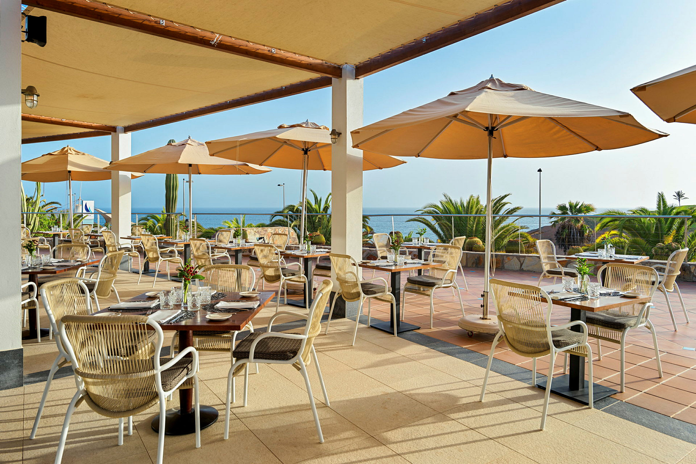 Restaurang med uteservering, bord och stolar under parasoller med utsikt över havet. (AI-genererad text)