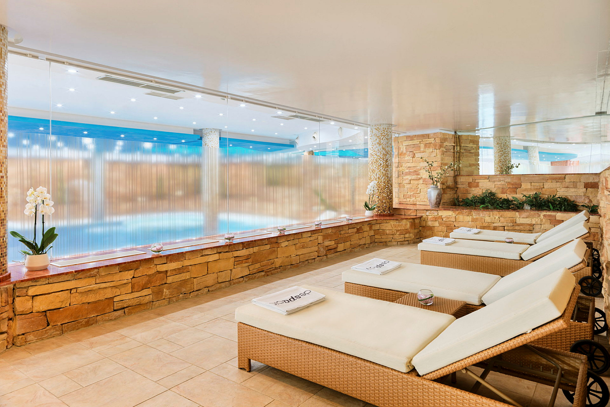 Ett avslappningsområde med vilstolar vid sidan av en pool, omgivet av stenbeklädda väggar. (AI-genererad text)
