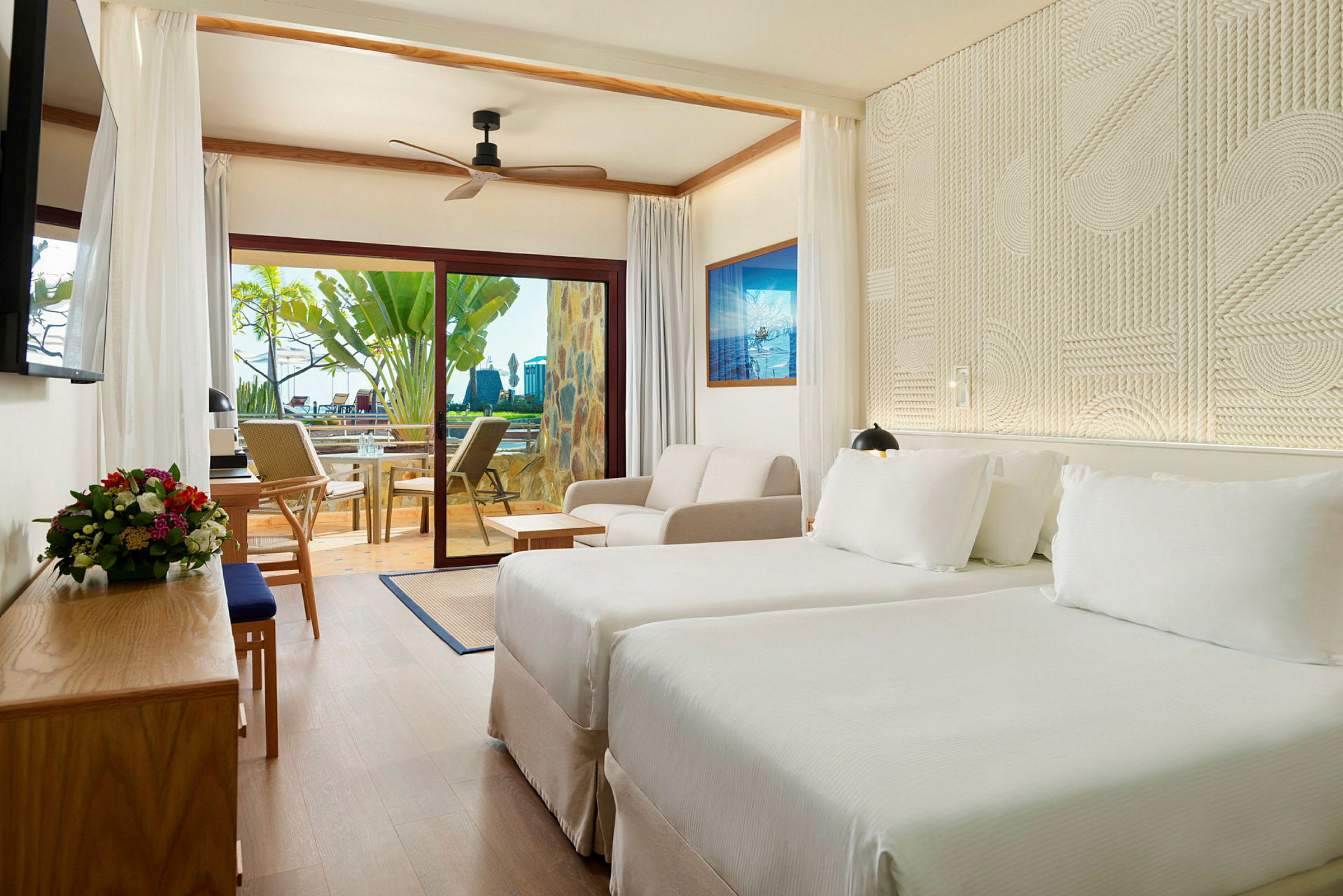 Hotellrum med två sängar, soffa och utsikt mot terrassen genom glasdörr. (AI-genererad text)