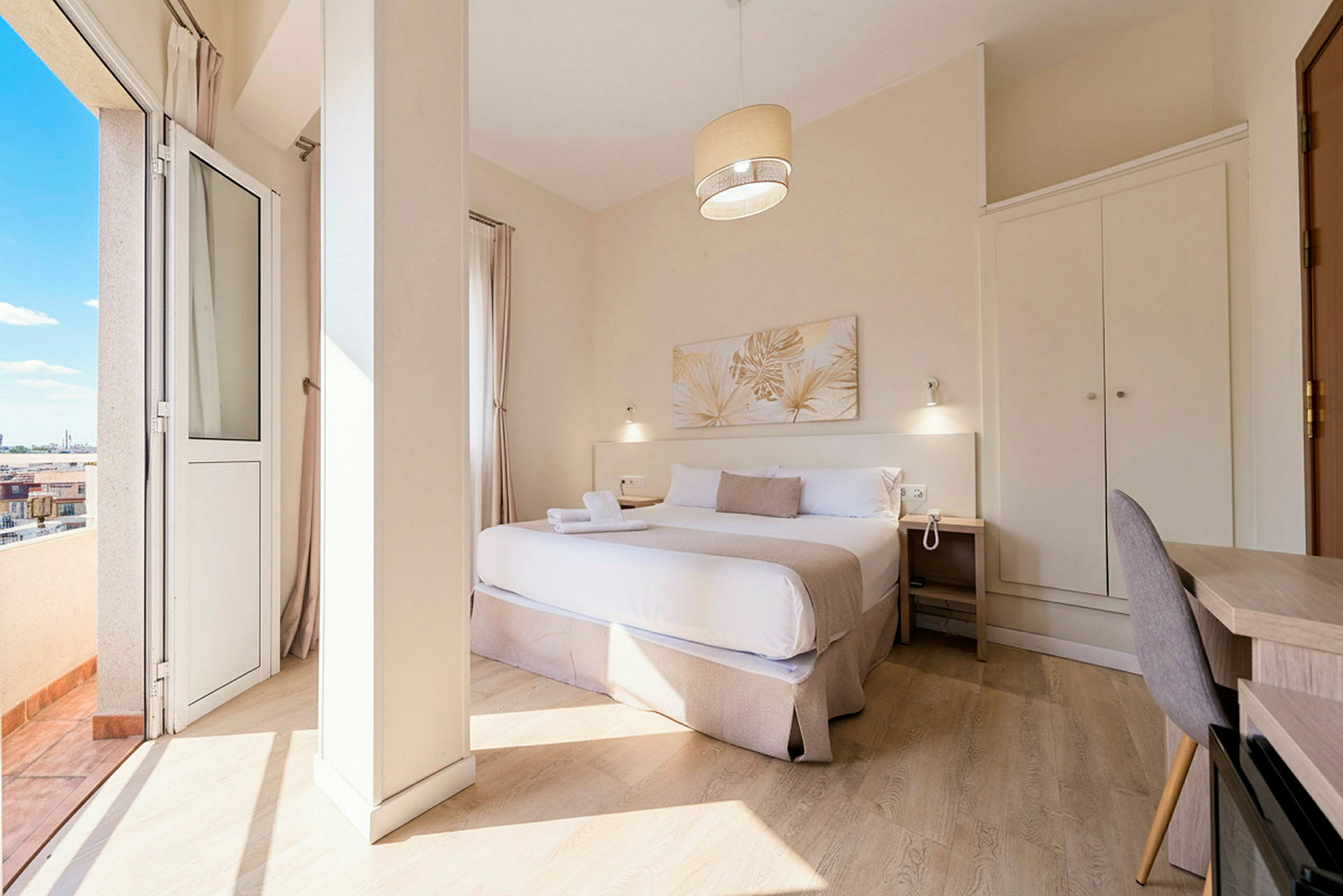 Ett hotellrum med en dubbelsäng, sängbord, skrivbord och garderob, samt en balkong med utsikt. (AI-genererad text)