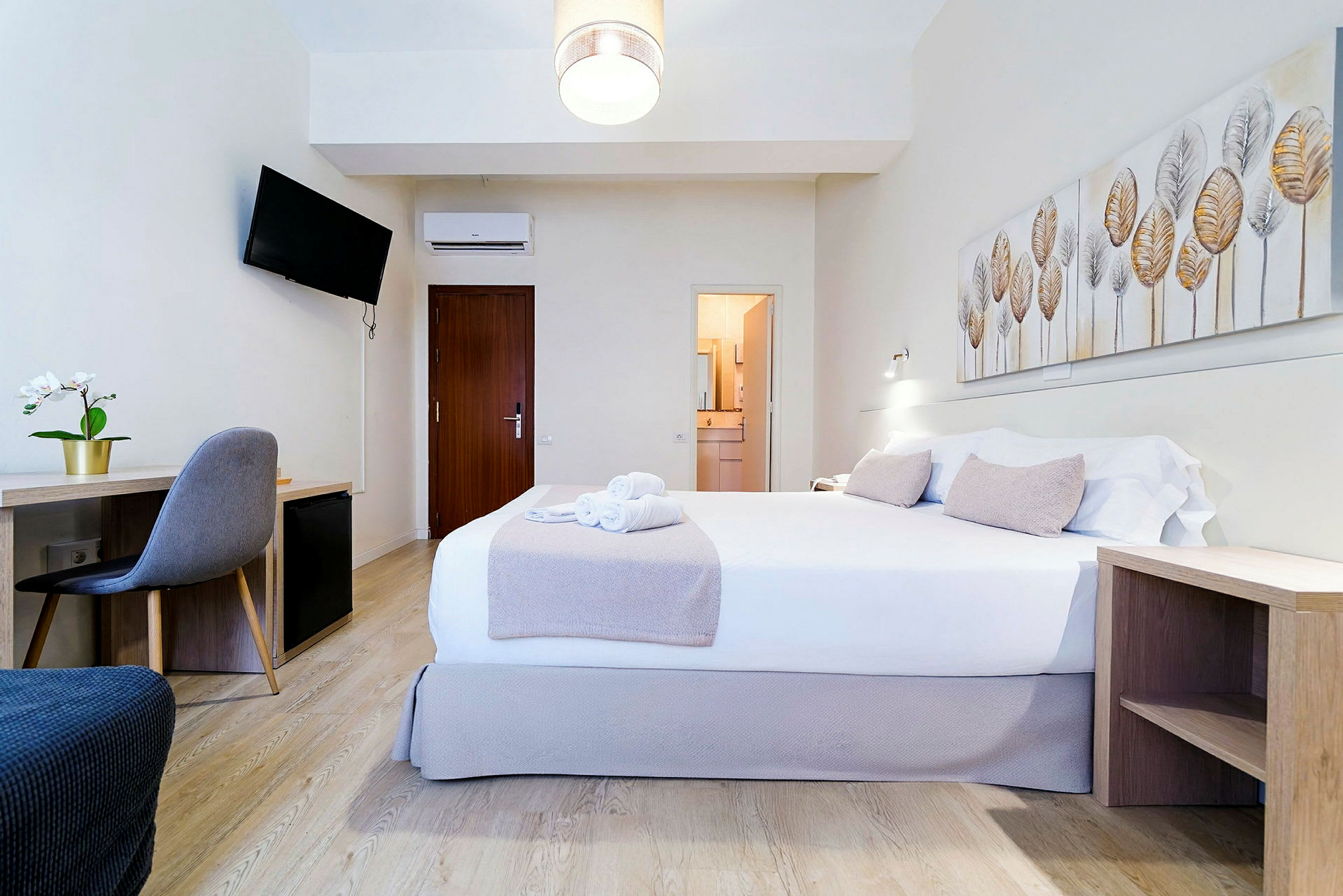 Ett hotellrum med en dubbelsäng, skrivbord, stol, och väggdekoration. (AI-genererad text)