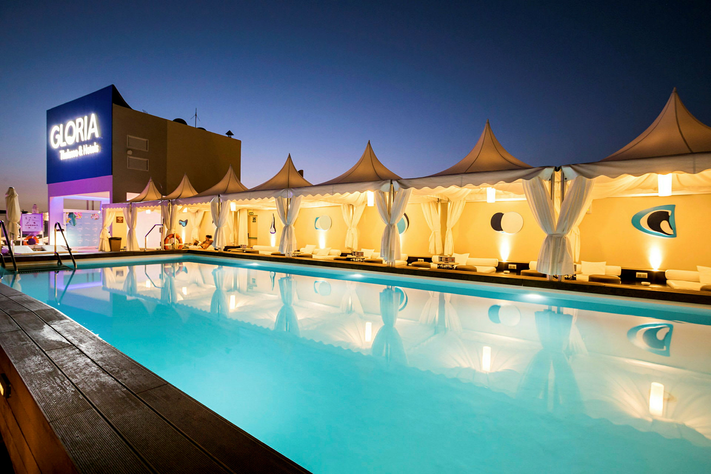 En pool omgiven av tält med belysning vid Gloria Palace. (AI-genererad text)
