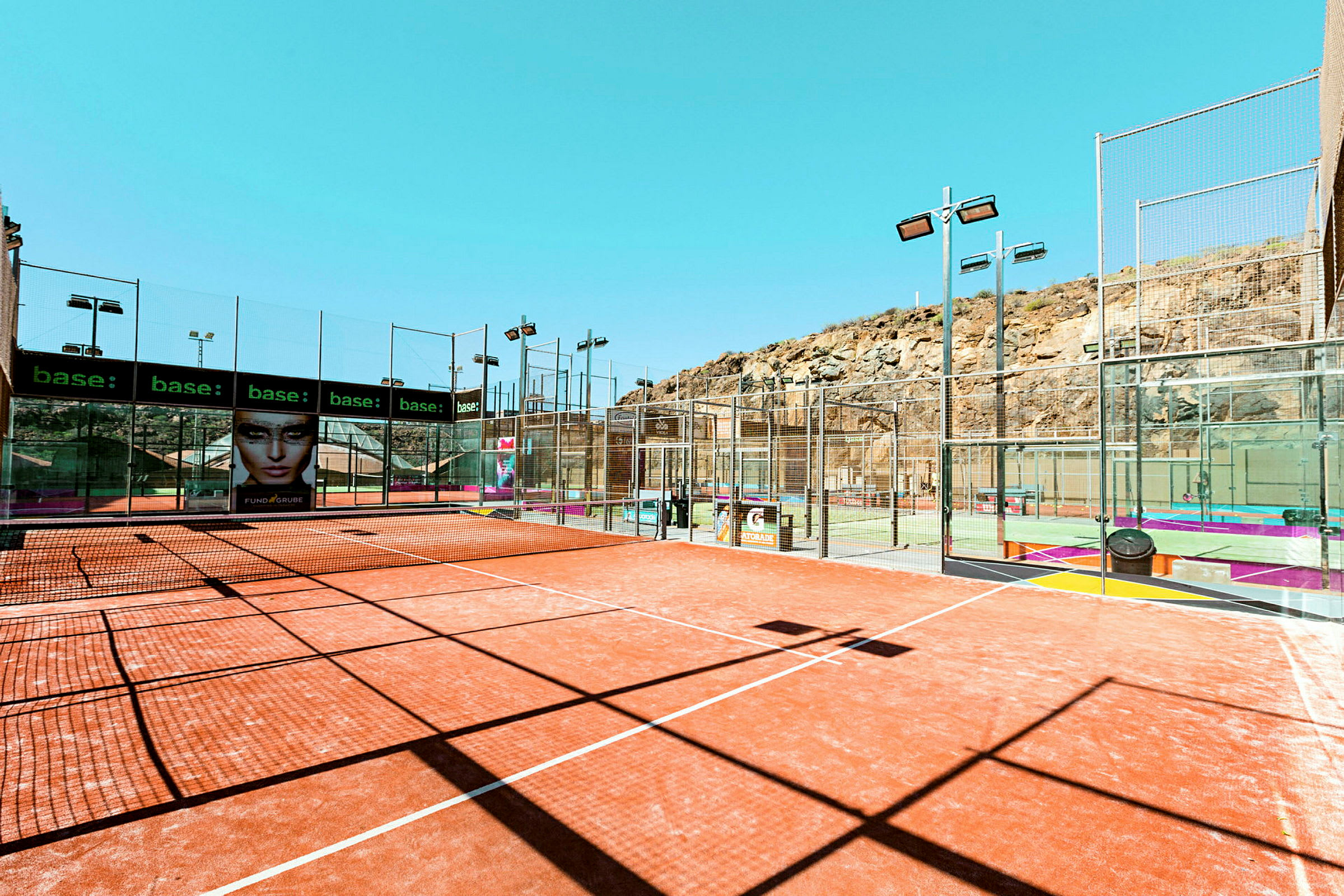 Padelbanor utomhus vid bergsterräng med nät och omgivande staket. (AI-genererad text)
